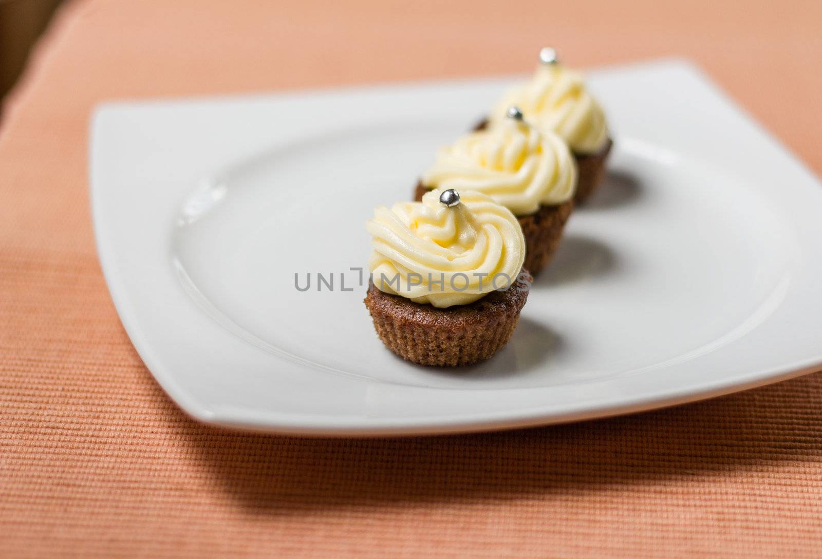 Three chocolate cupcakes with silver sprinkles on top, on white plate and fabric tablecloth
