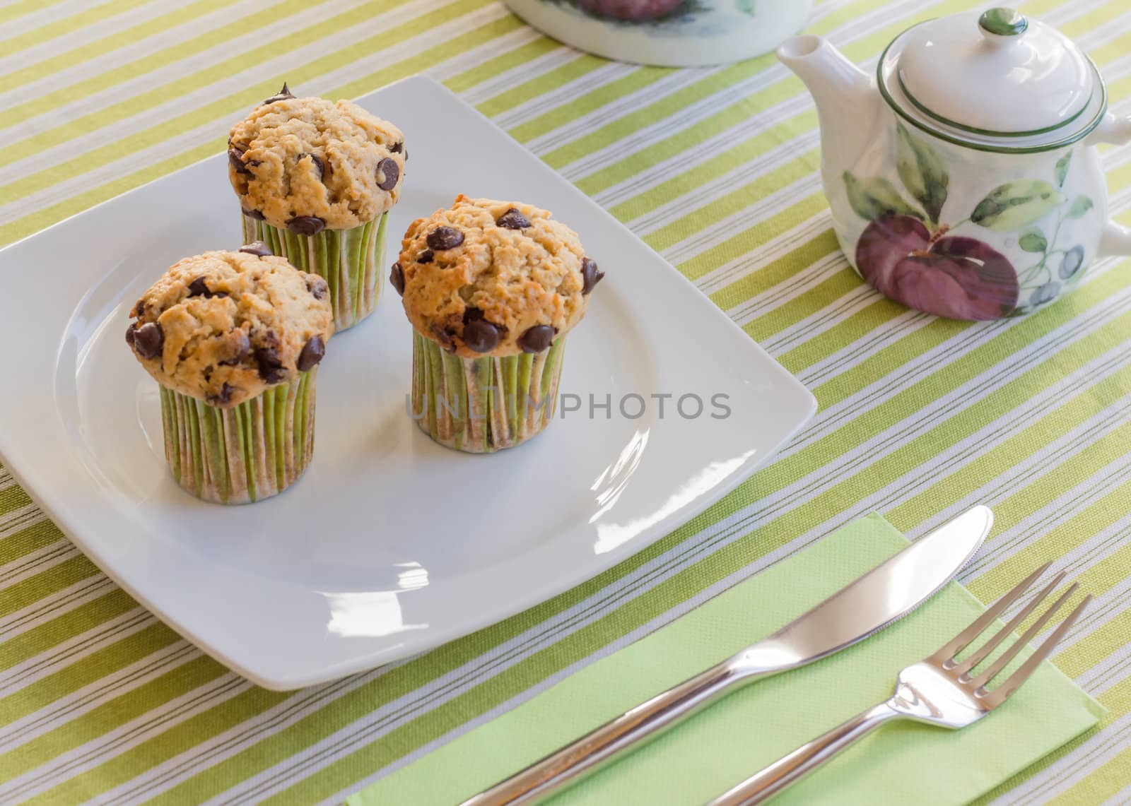 Chocolate chip muffins on white plate and green striped tableclo by doble.d