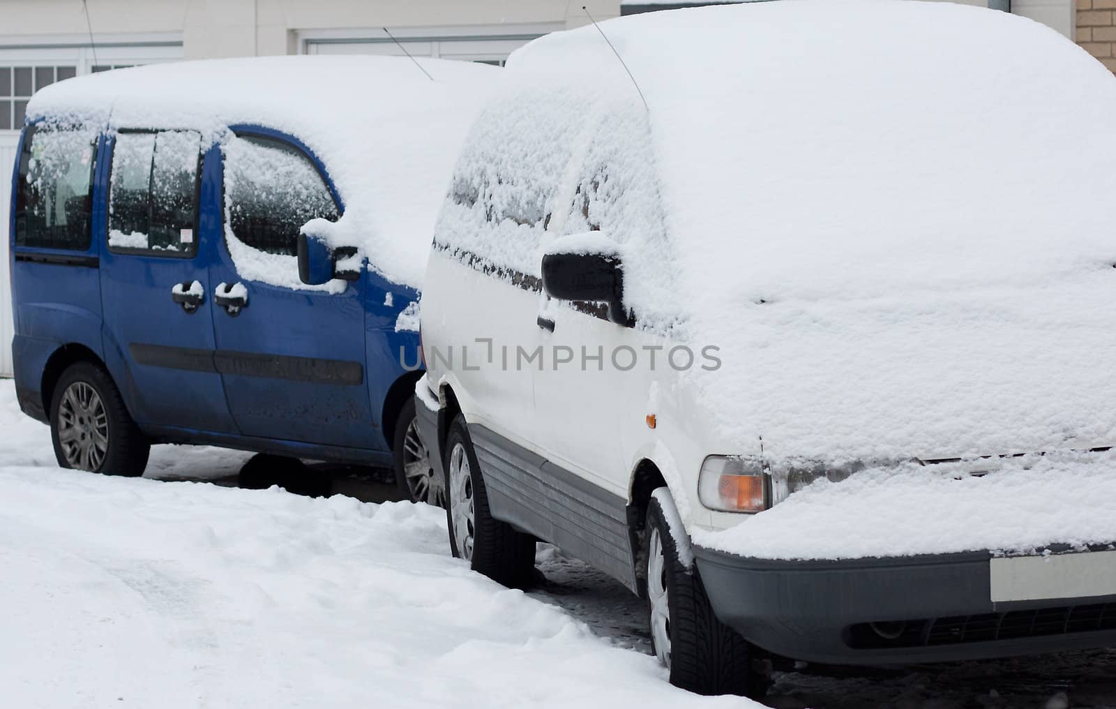 Two cars covered in snow during a snowfall in town.