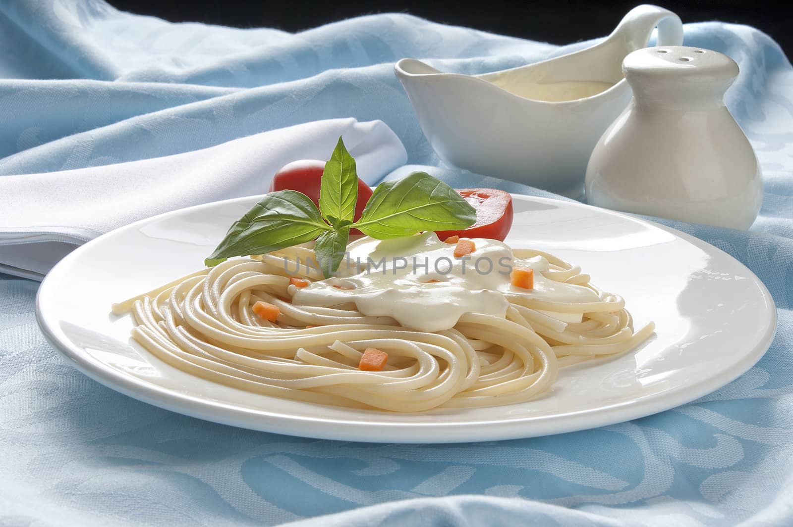 Spaghetti with cheese-cream sauce, tomato and basil on the white plate