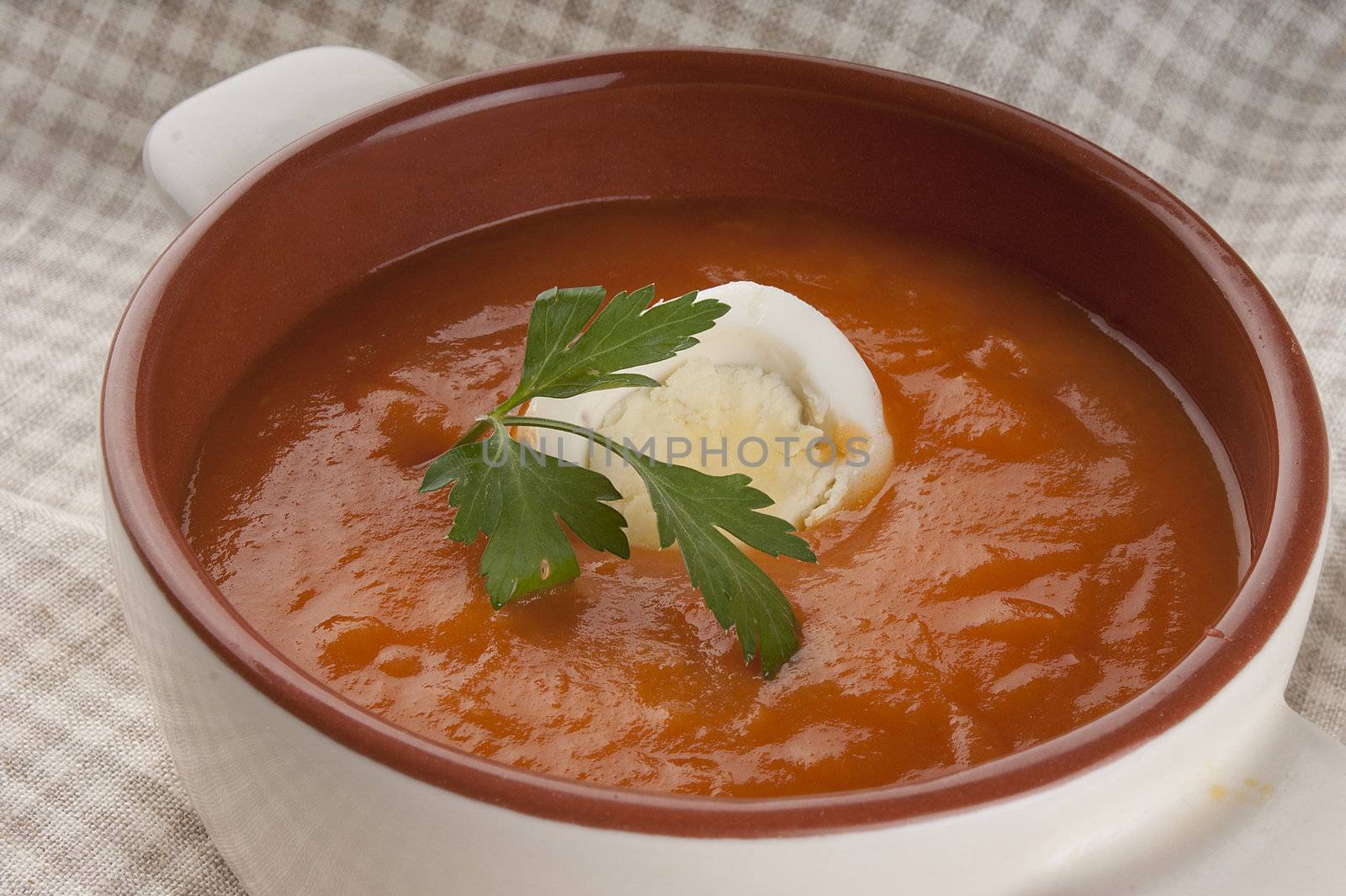 Tomato soup with parsley and boiled egg in white bowl