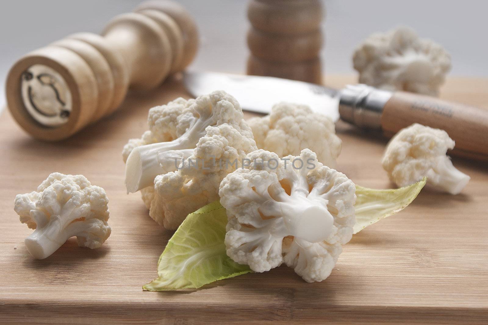 Pieces of cauliflower on the wooden board with knife and pepper mill