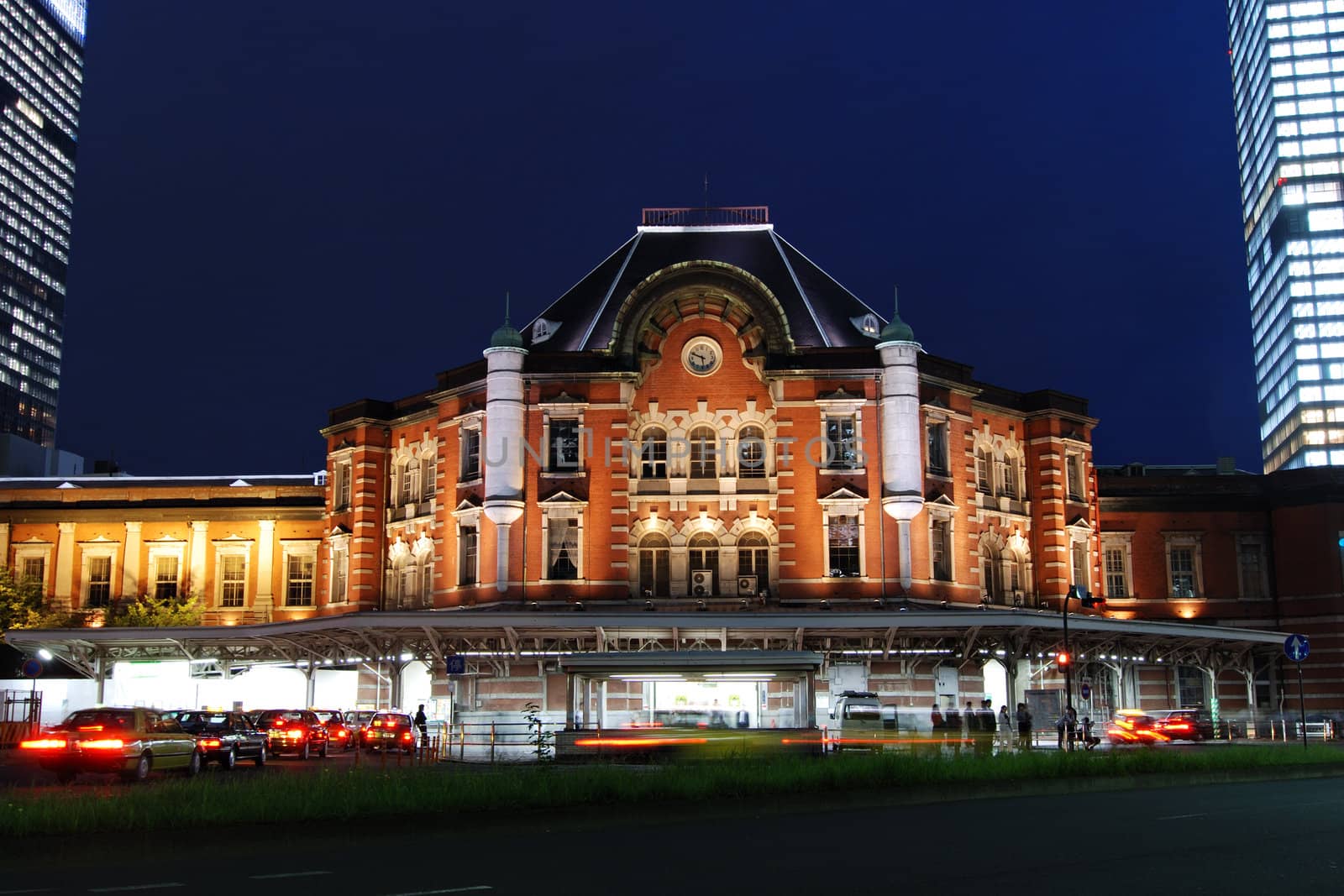 old building of Tokyo railway station built in 1914 at twilight time with many taxi-cars among huge modern buildings, Japan