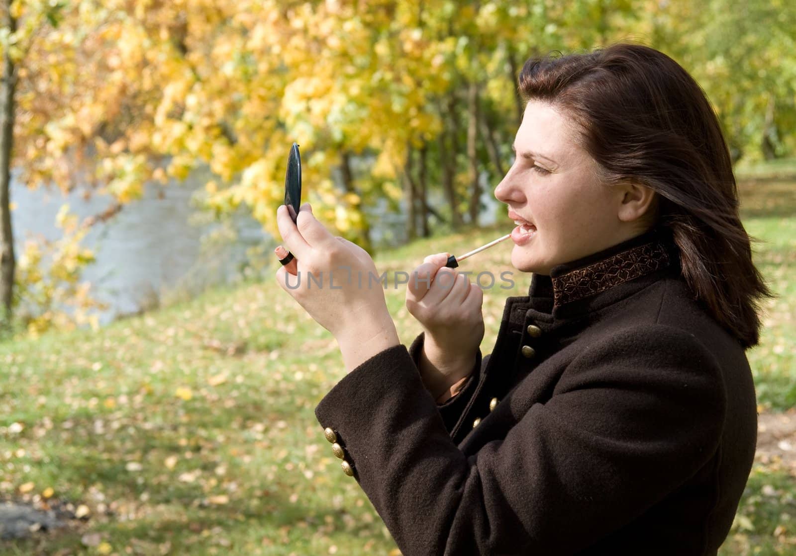 Autumn. Beautiful young woman put on lipstick.