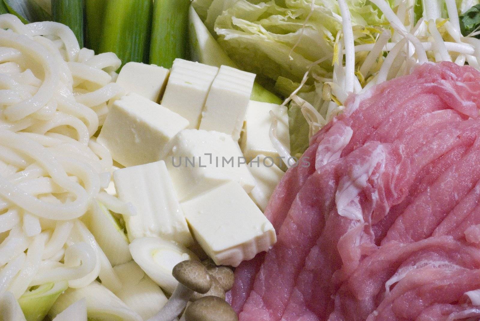 Noodles, tofu, pork and other ingredients spread out prepared for shabu shabu. white and red horizontal