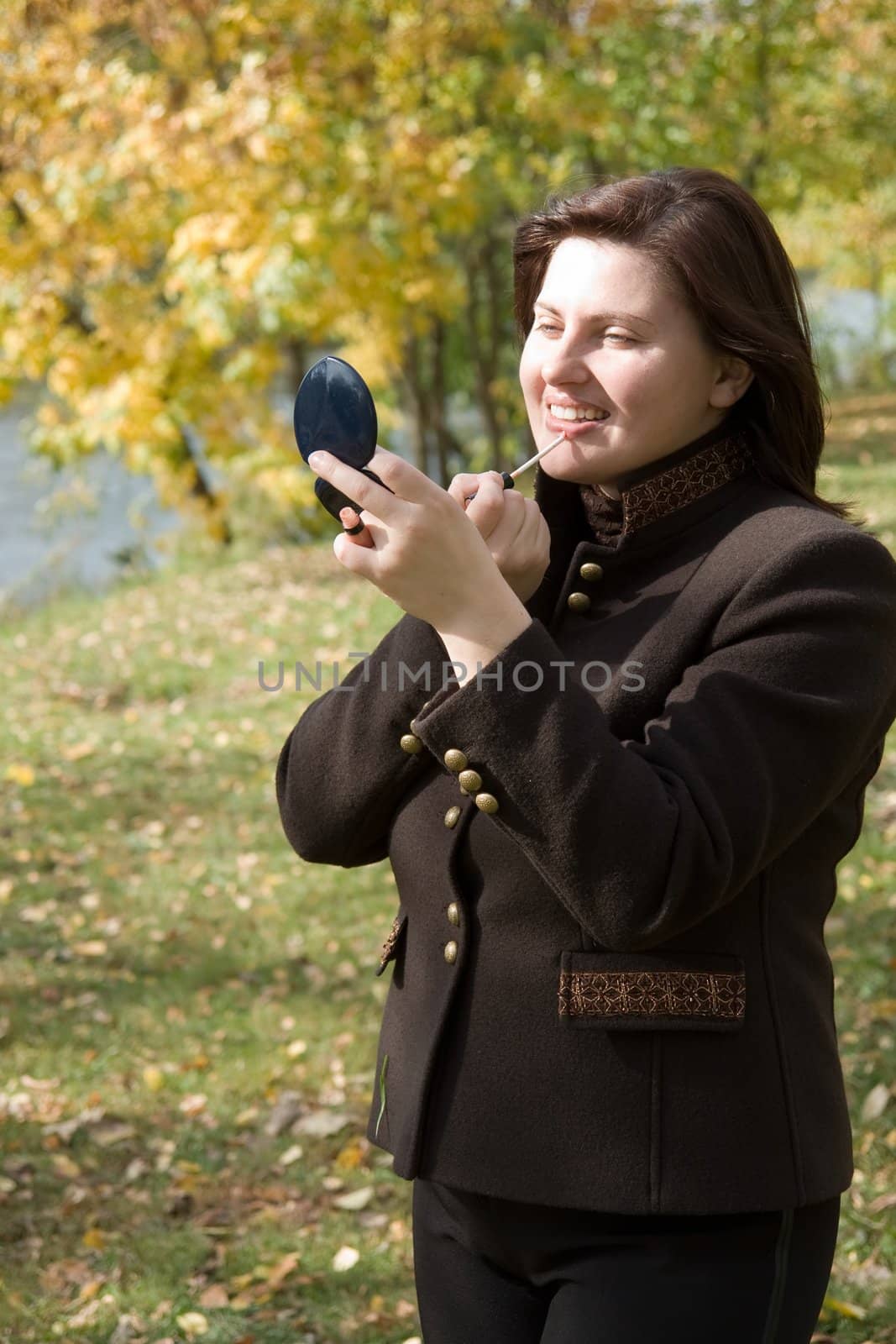 Autumn. Beautiful young woman put on lipstick.