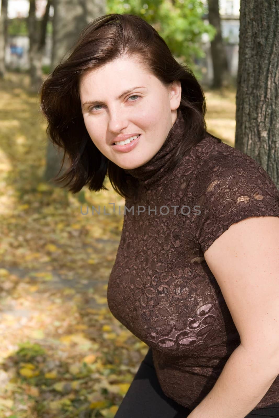 Smiling beautiful woman near a tree in autumn park.