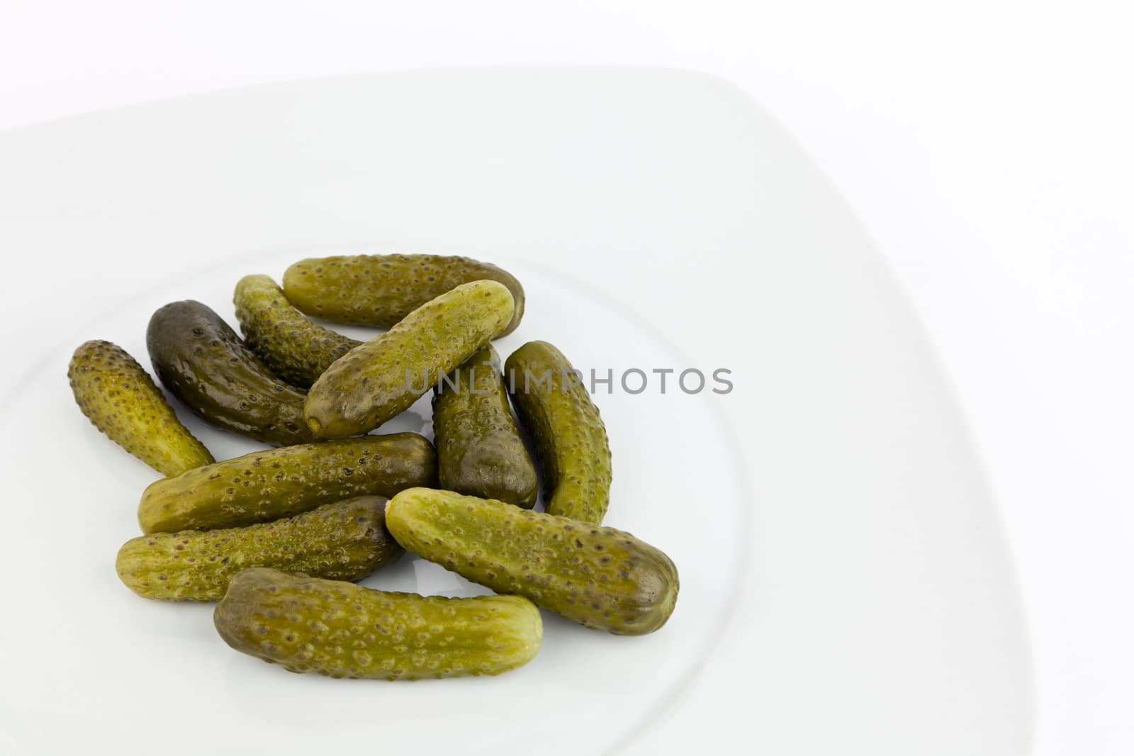 Pickled cucumbers in dish on white background.