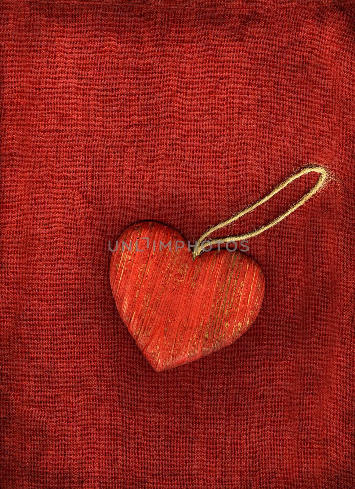 Red wooden heart with string on red background.