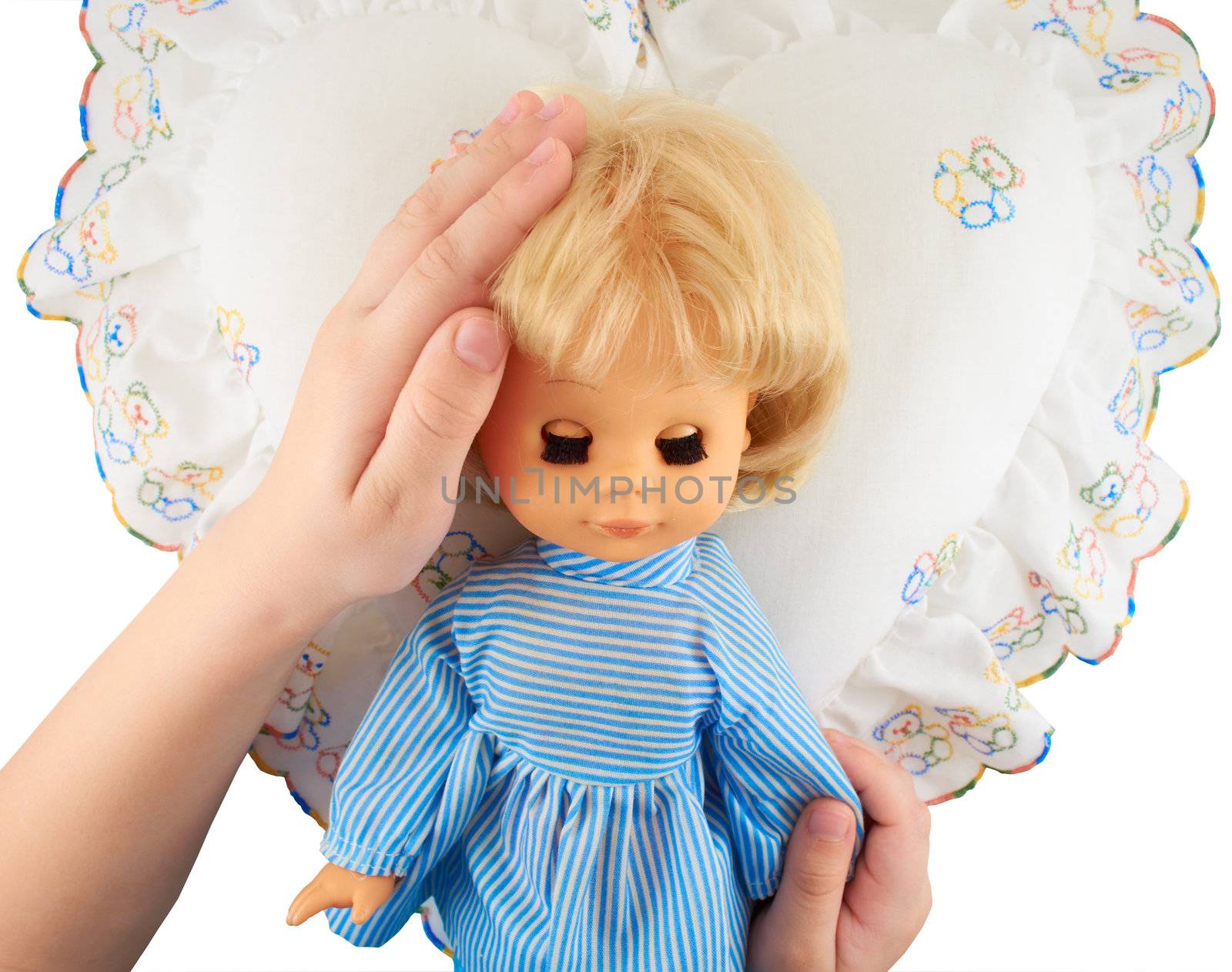Children's hands holding a doll lying on the pillow