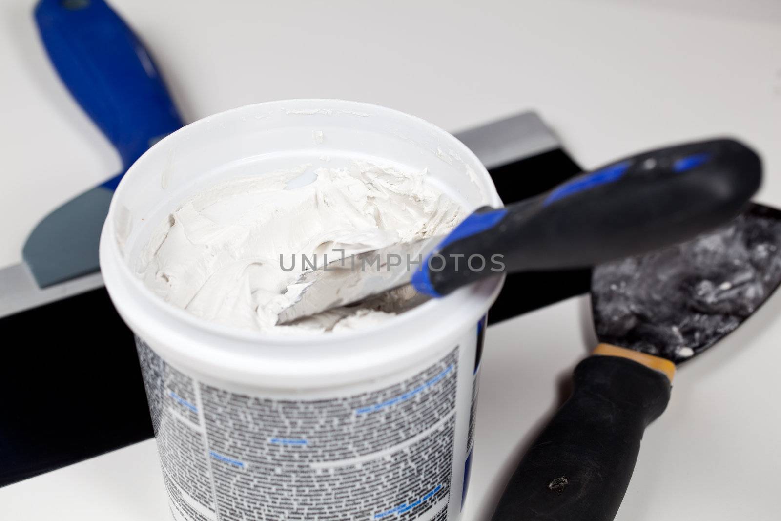 Knife in patching plaster in plastic tube with other tools on the floor