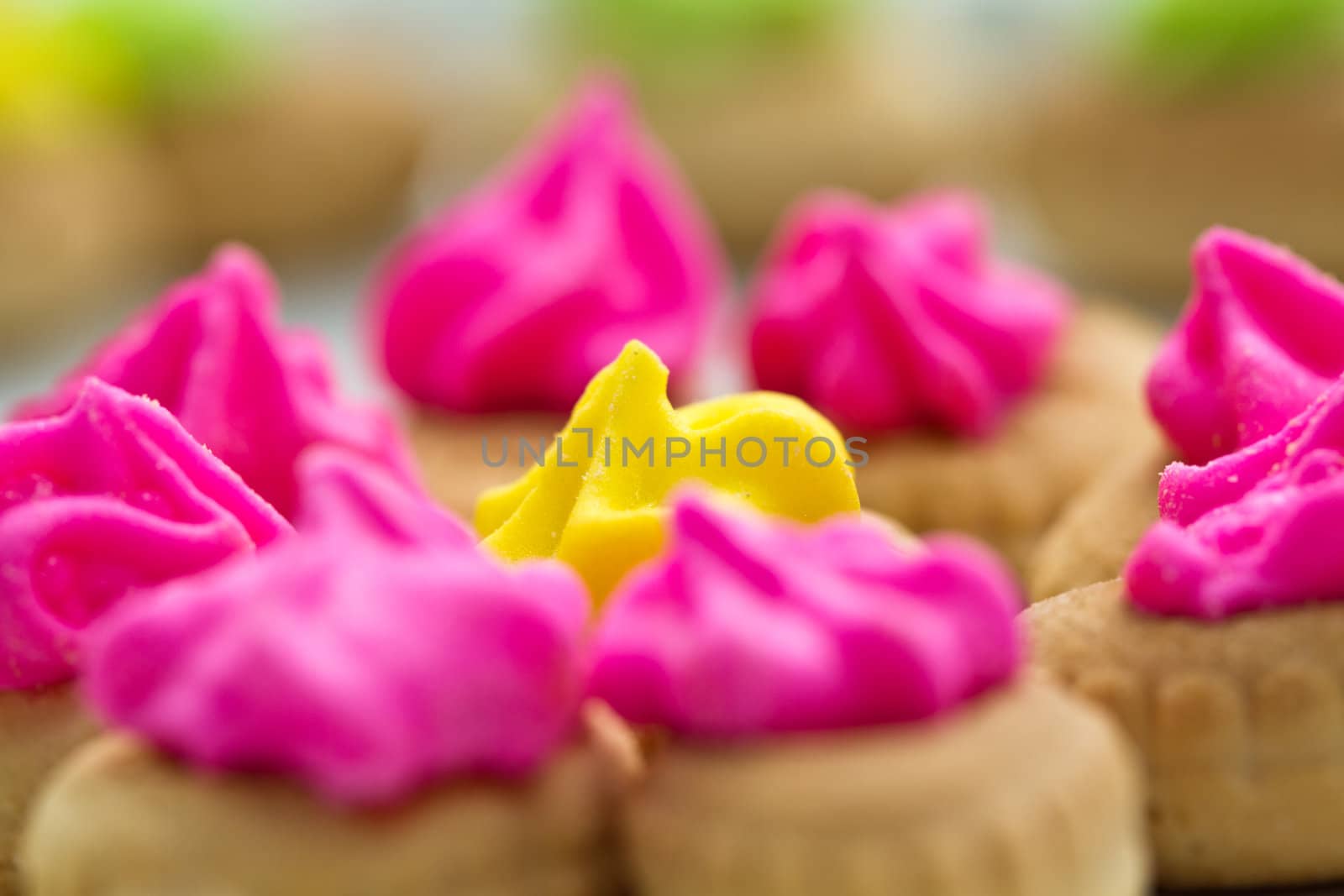 Close up view of the pink color icing topped cookies surrounding the yellow with green icing cookies in background