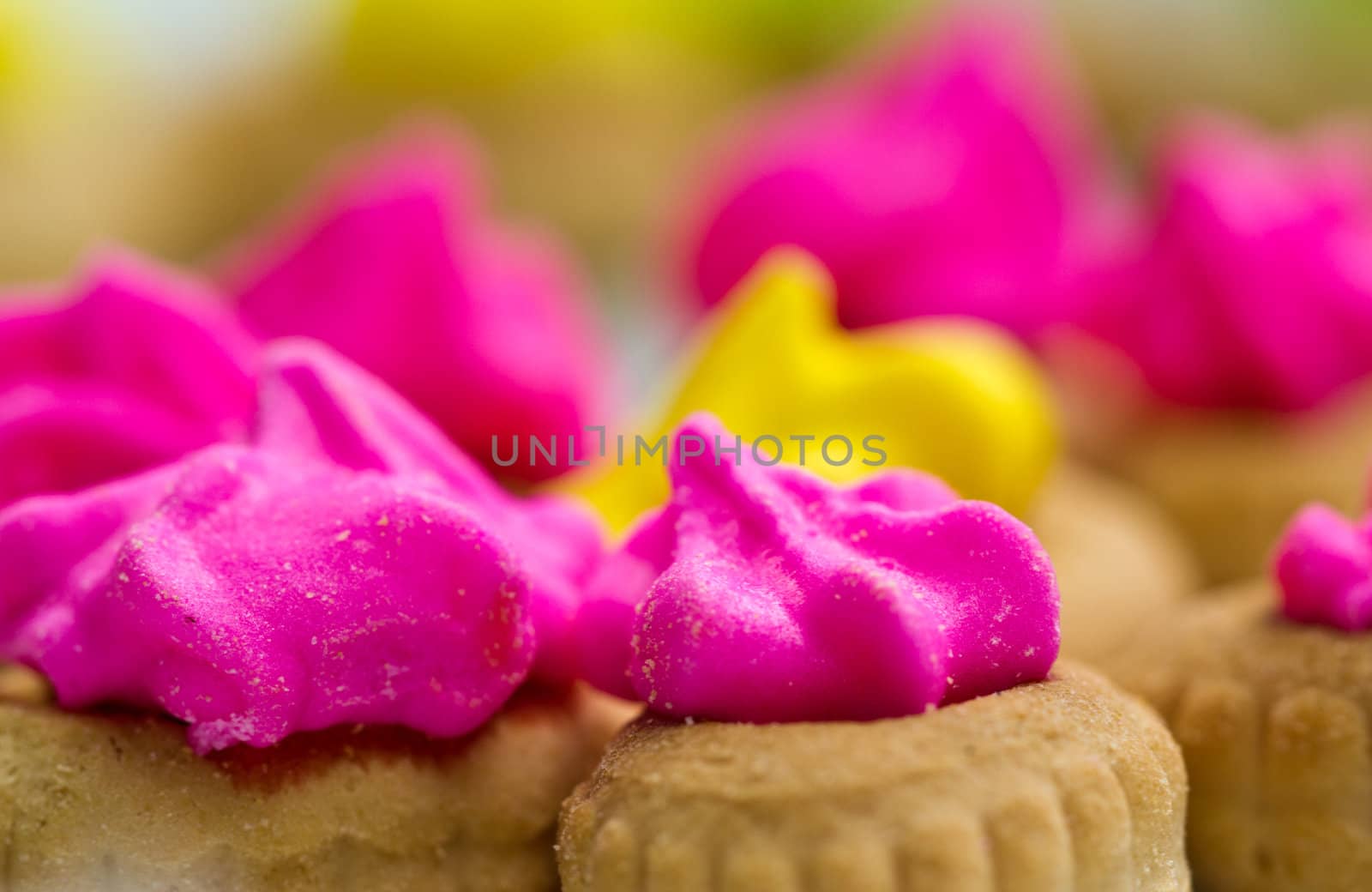 Close up view of the pink color icing topped cookies surrounding the yellow with green icing cookies in background