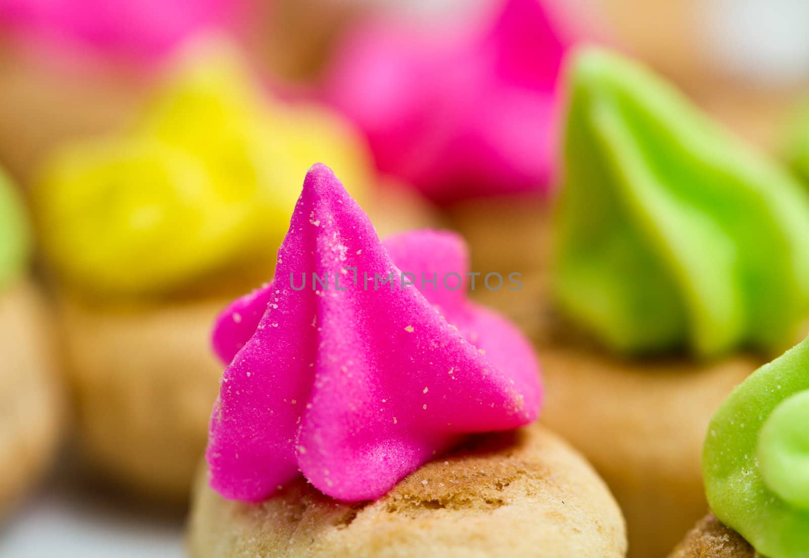 Close up view of the pink color icing topped cookies with green and yellow icing cookies in background