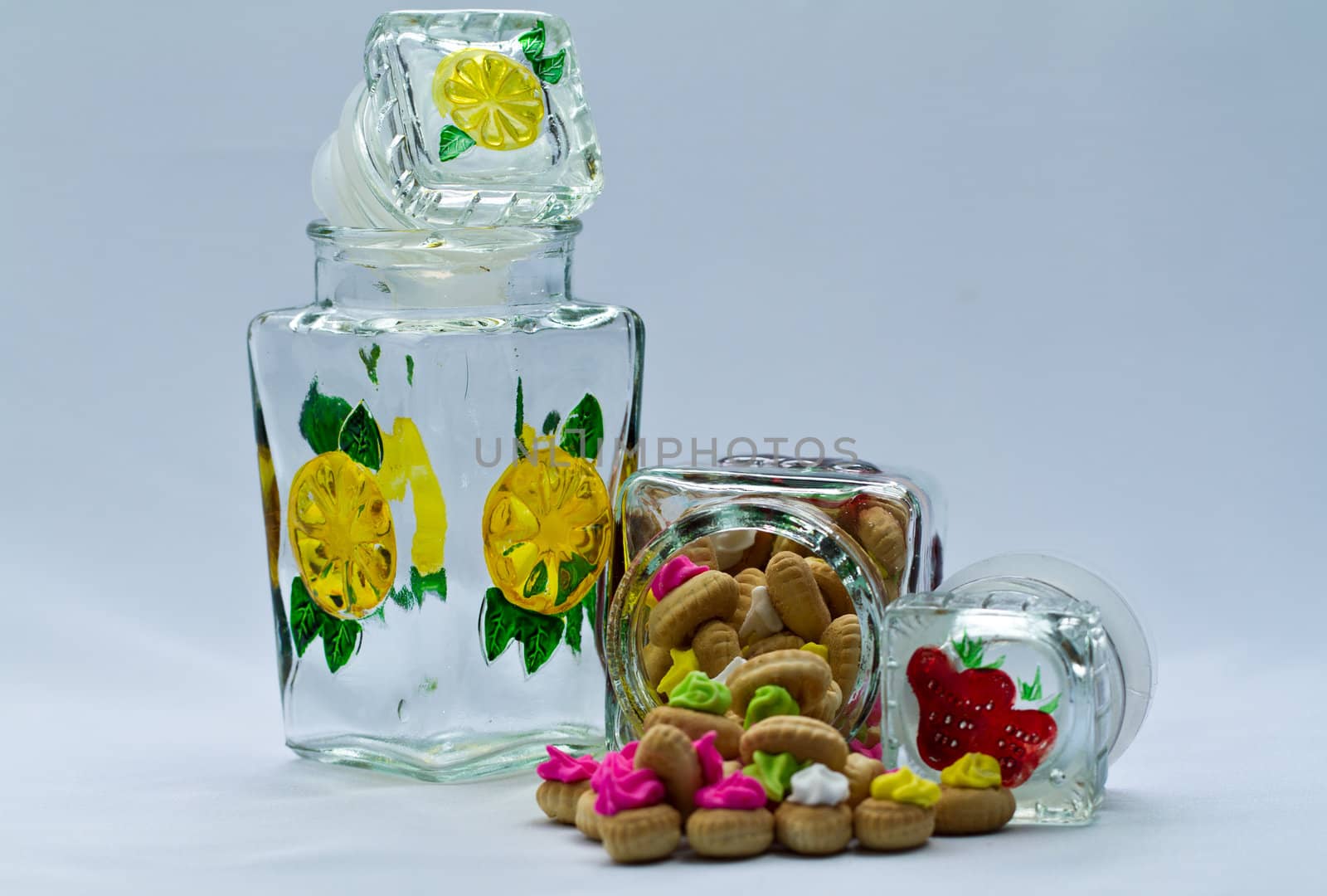 icing topped cookies spilled from a glass jar on bluish surface and background in landscape orientation