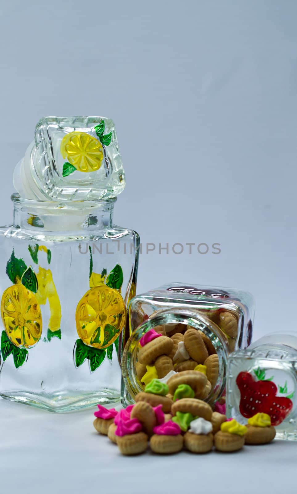icing topped cookies spilled from a glass jar on bluish surface and background in portrait orientation