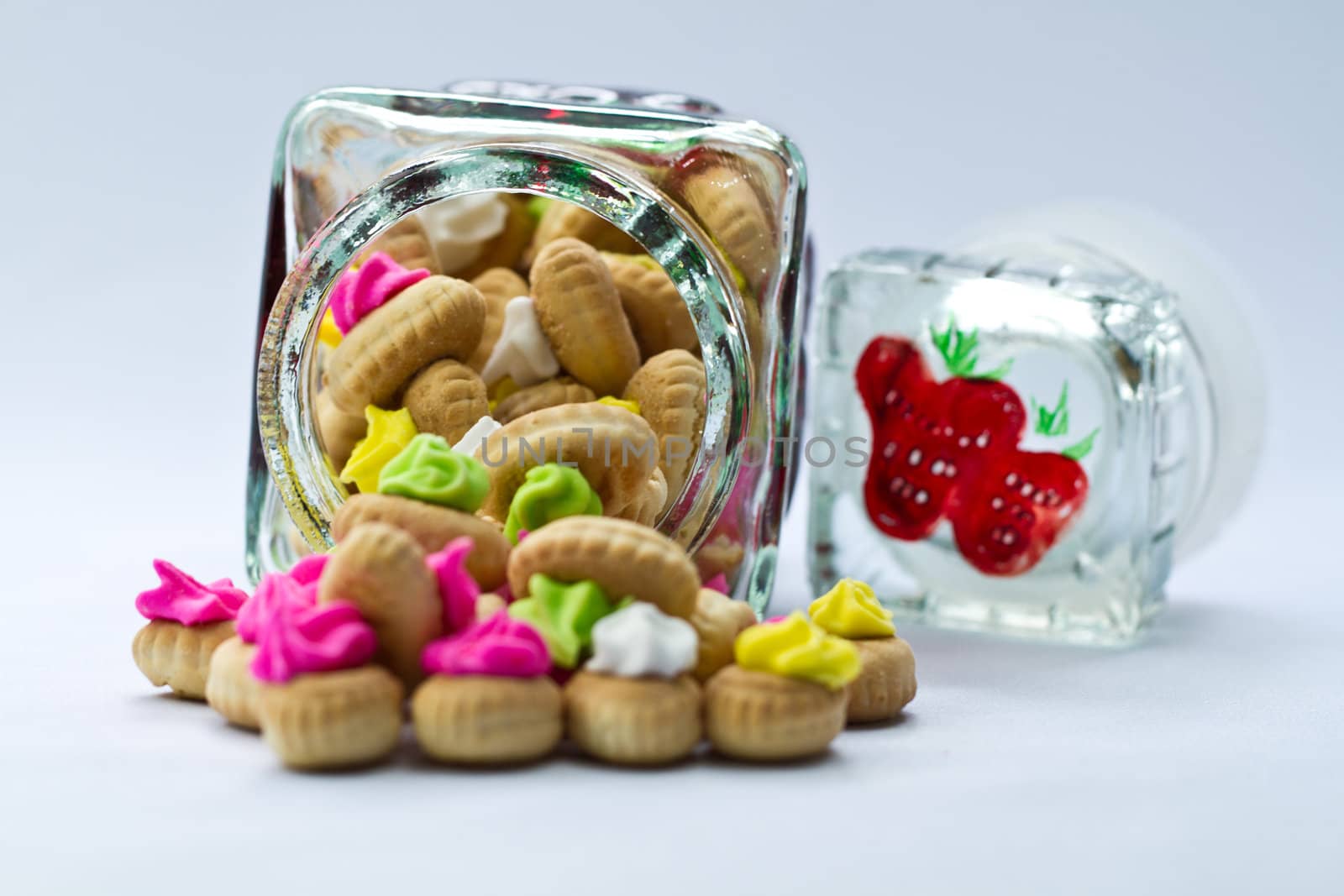 Icing topped cookies spilled from a glass jar on bluish surface and background in landscape orientation