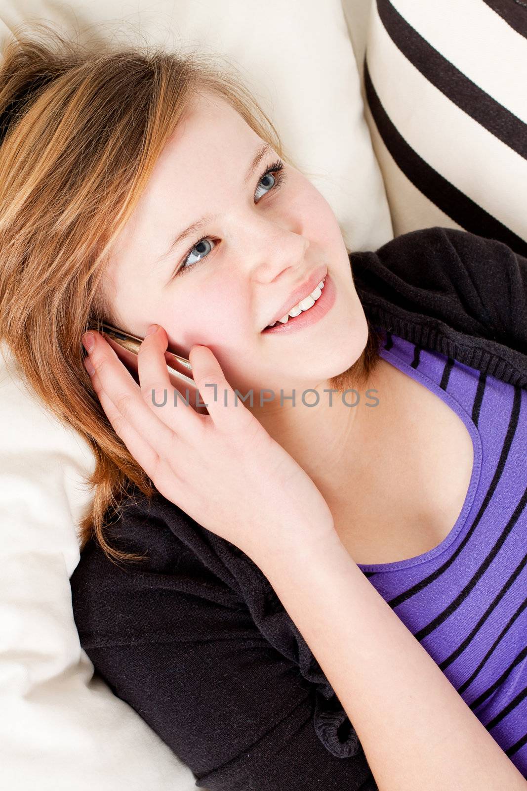 teenager girl smiling and lying on couch with mobile phone and talking