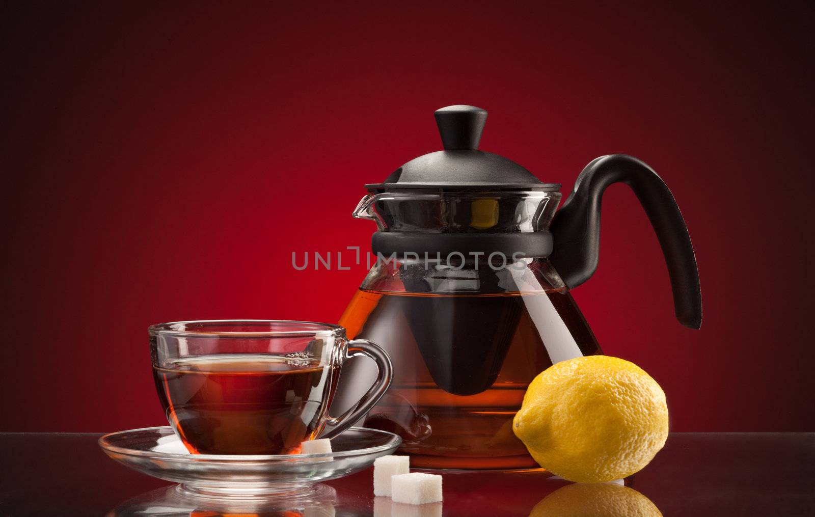 glassy teacup and teapot with tea and lemon over red