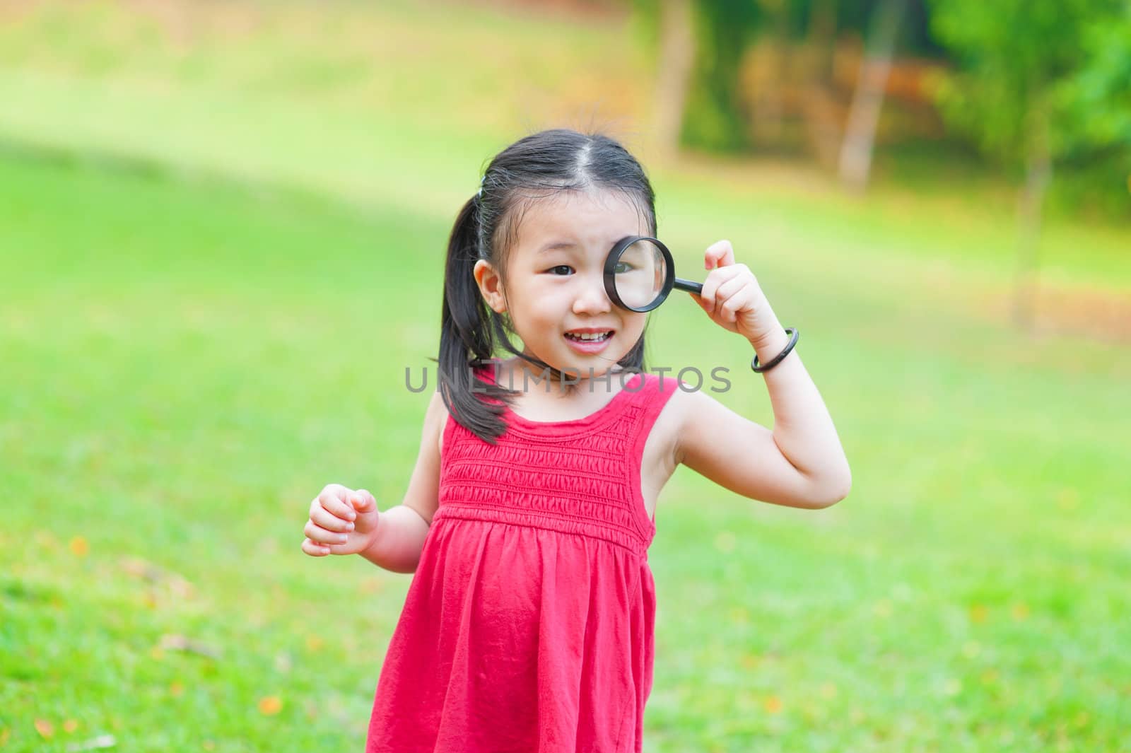 Little Asian girl exploring nature by magnifier glass