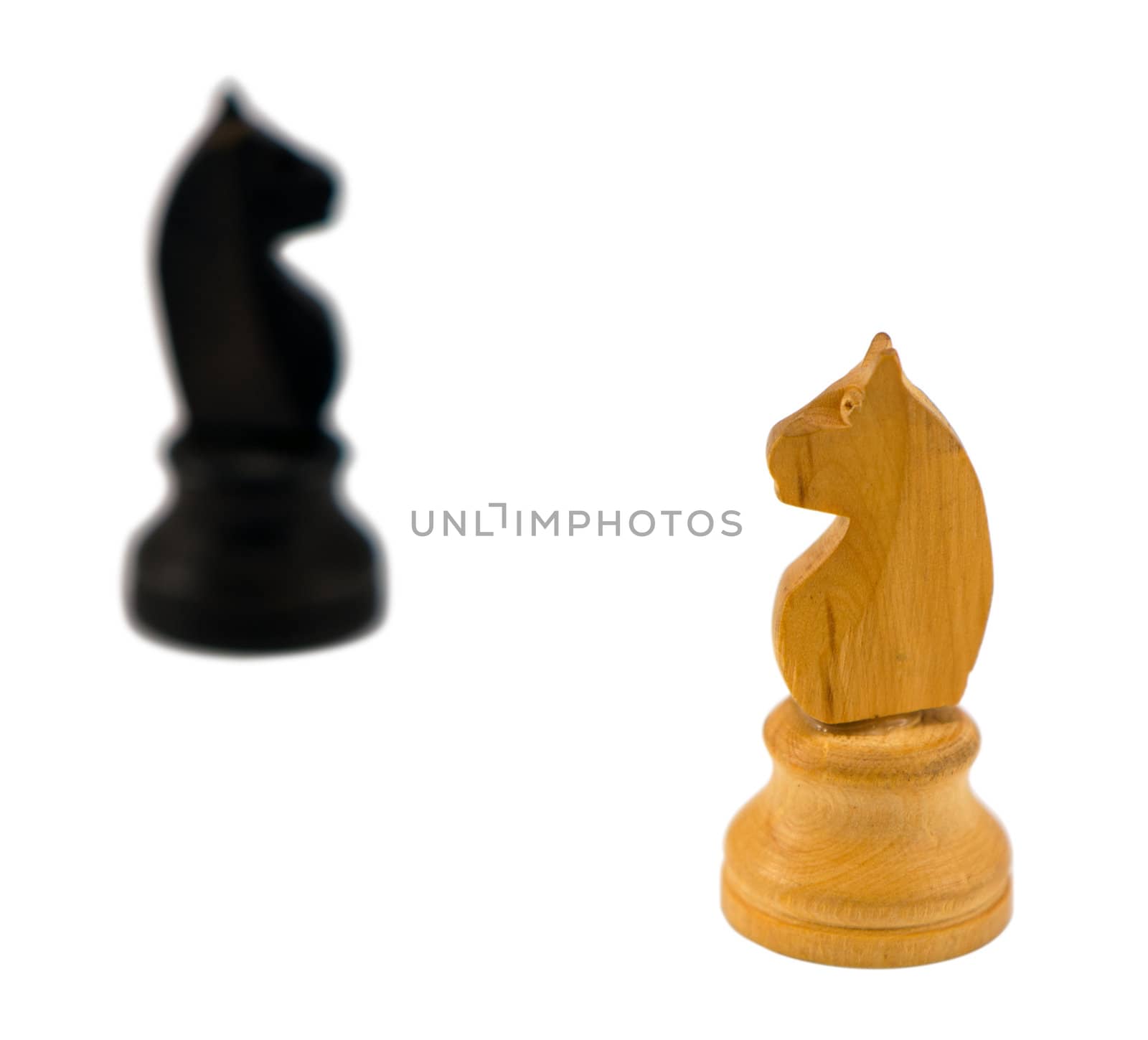 white wooden chess knight figure and blurred black one in distance on white background