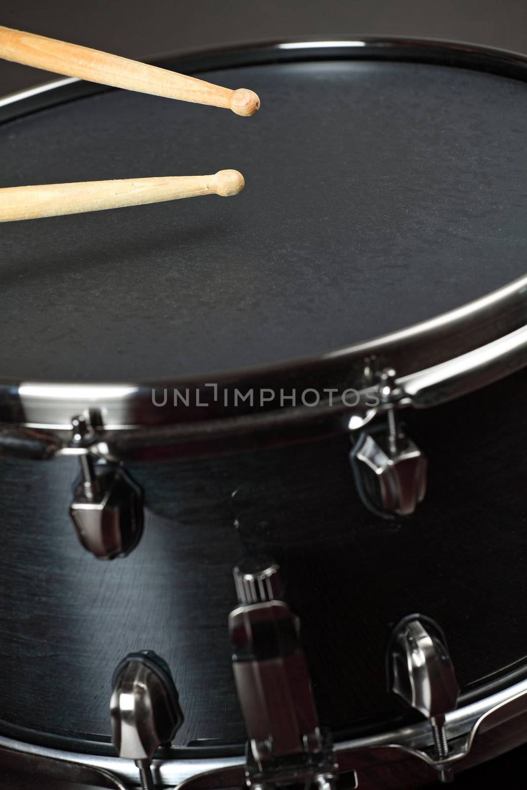 Drumsticks playing on a wood snare with black drum skin.