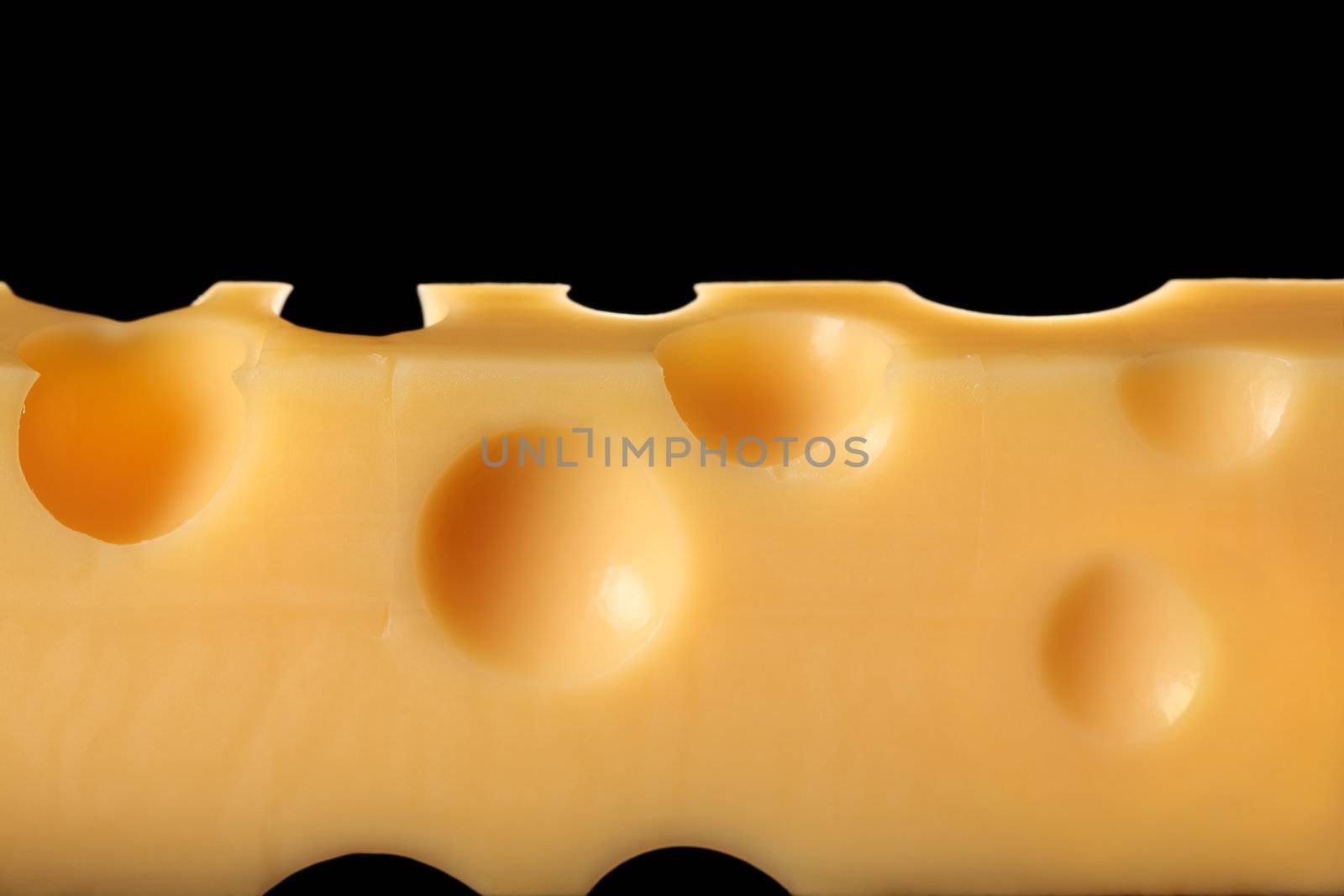 Macro photo of a block of Emmentaler cheese from Switzerland.  Backlit over a black background.