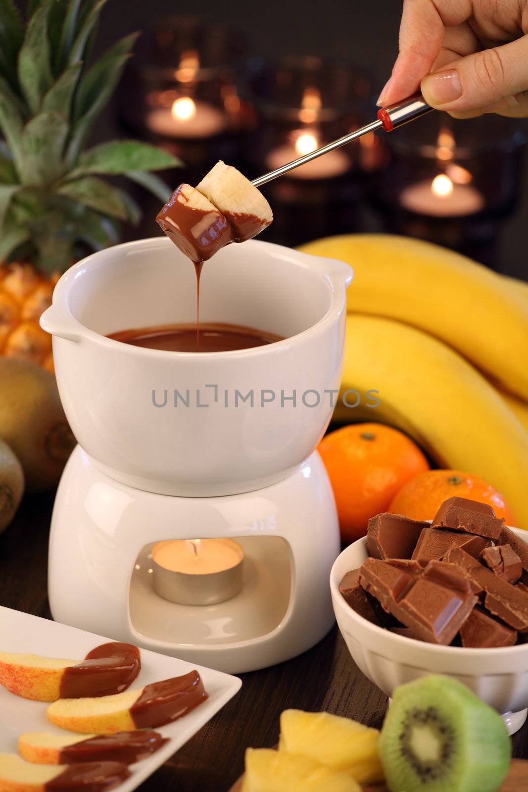 Photo of bananas being dipped into the bowl of the chocolate fondue. Selective focus on the bananas.