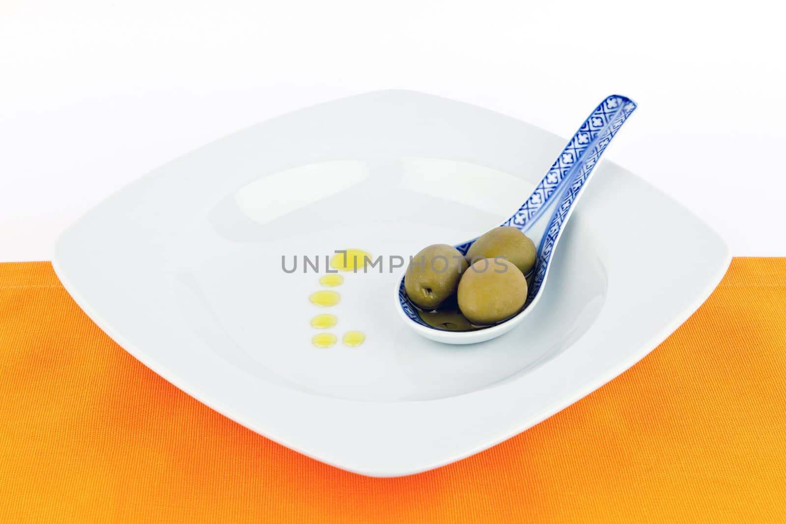 Spoon with olives and olive oil isolated on white and orange.