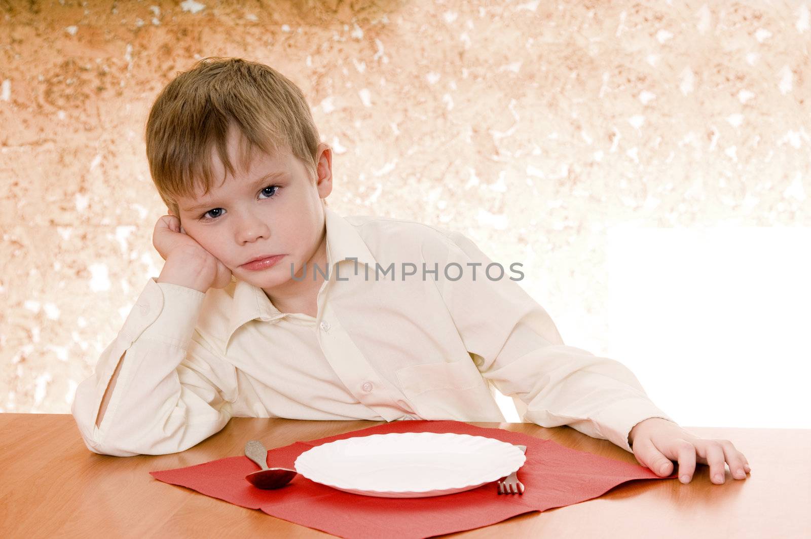 pensive child sits near an empty plate and  looks ahead