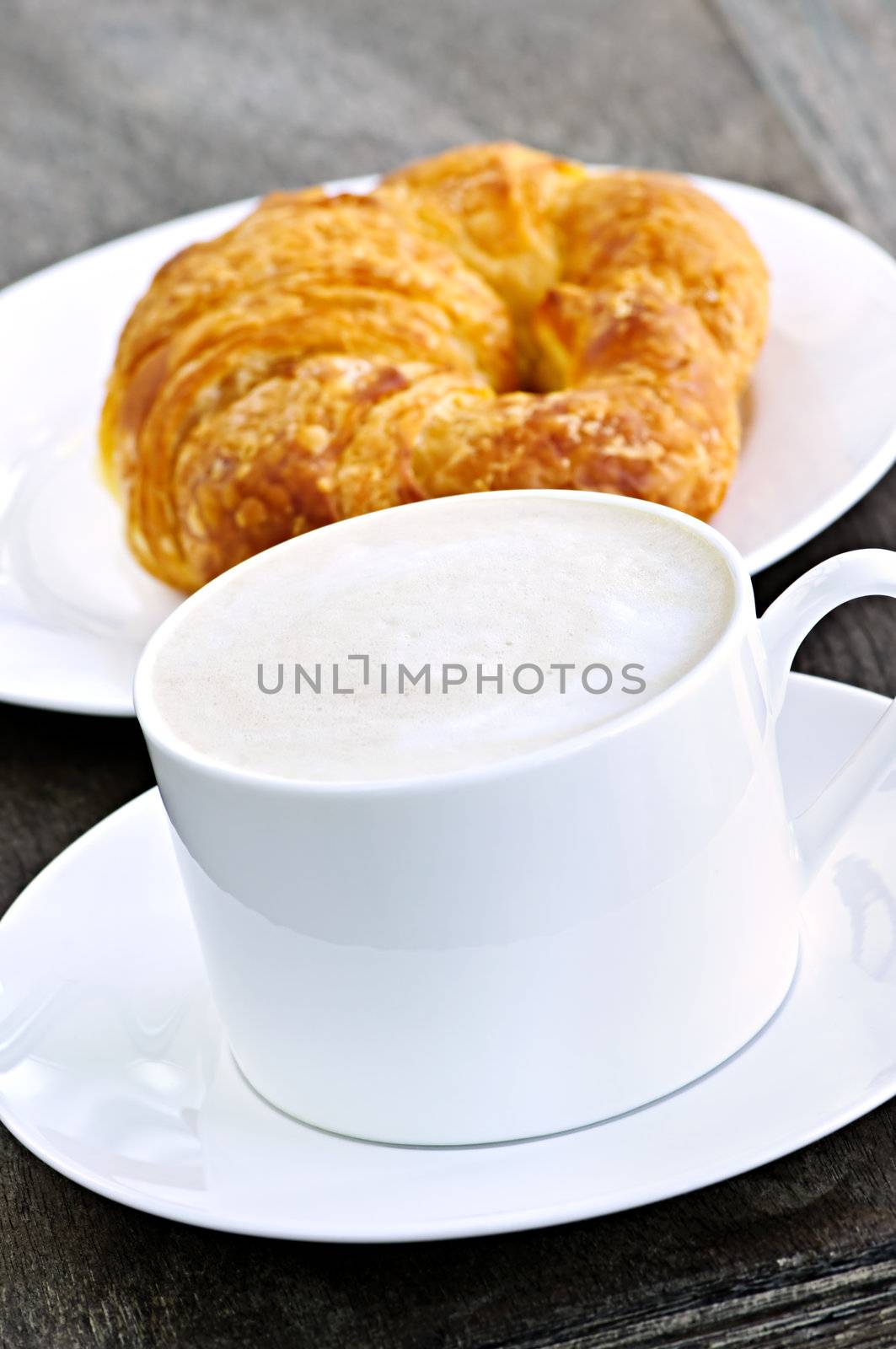 Latte coffee with frothed milk and fresh croissant