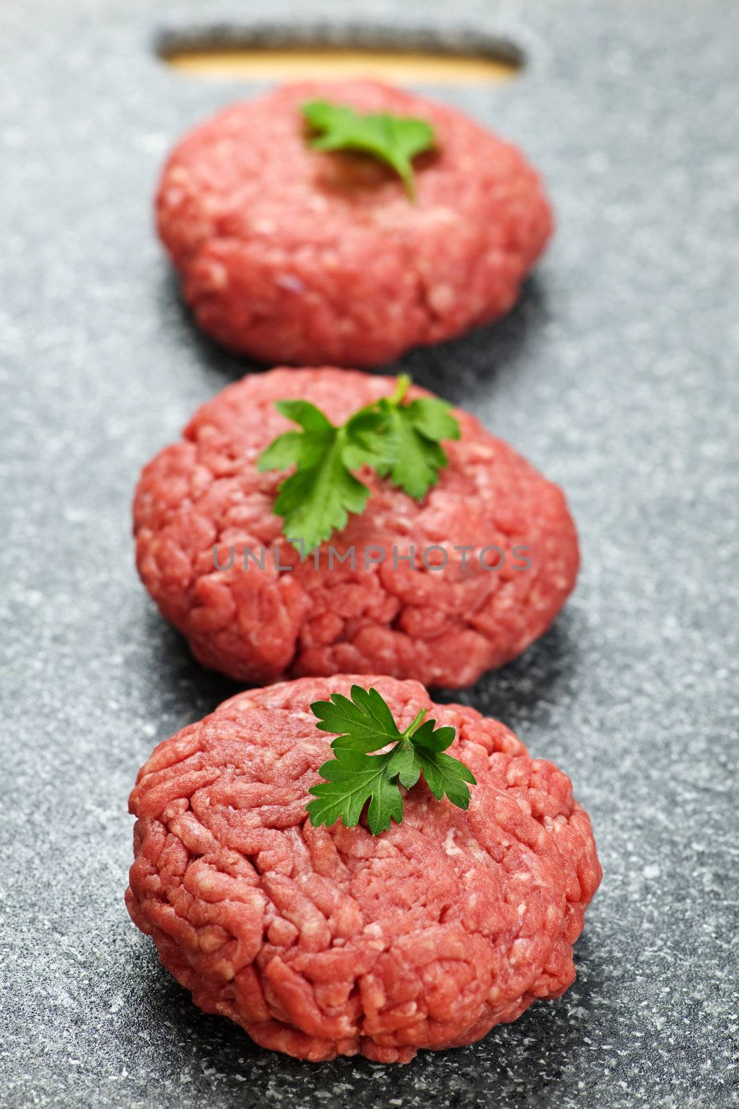 Three ground beef hamburger patties on cutting board