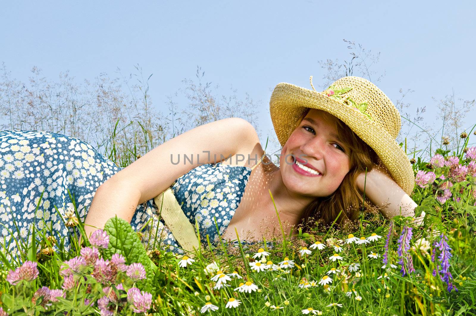 Young teenage girl laying on summer meadow amid wildflowers in straw hat