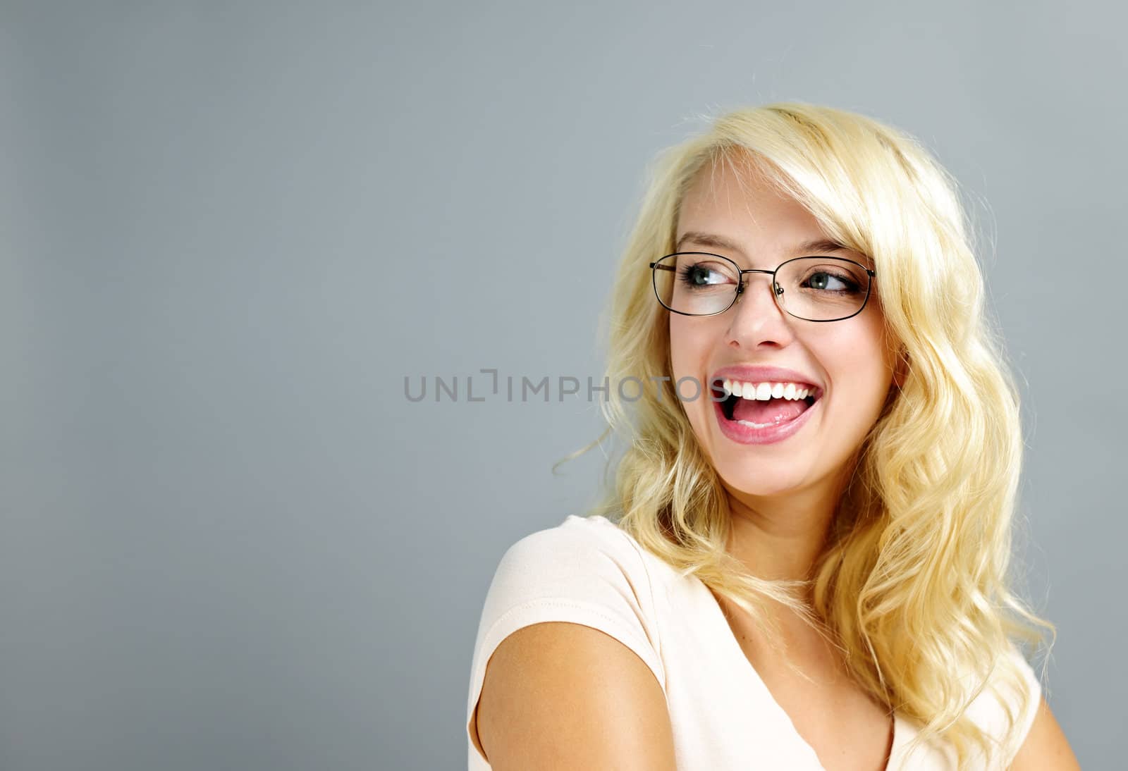 Happy young woman wearing eyeglasses looking to the side on grey background