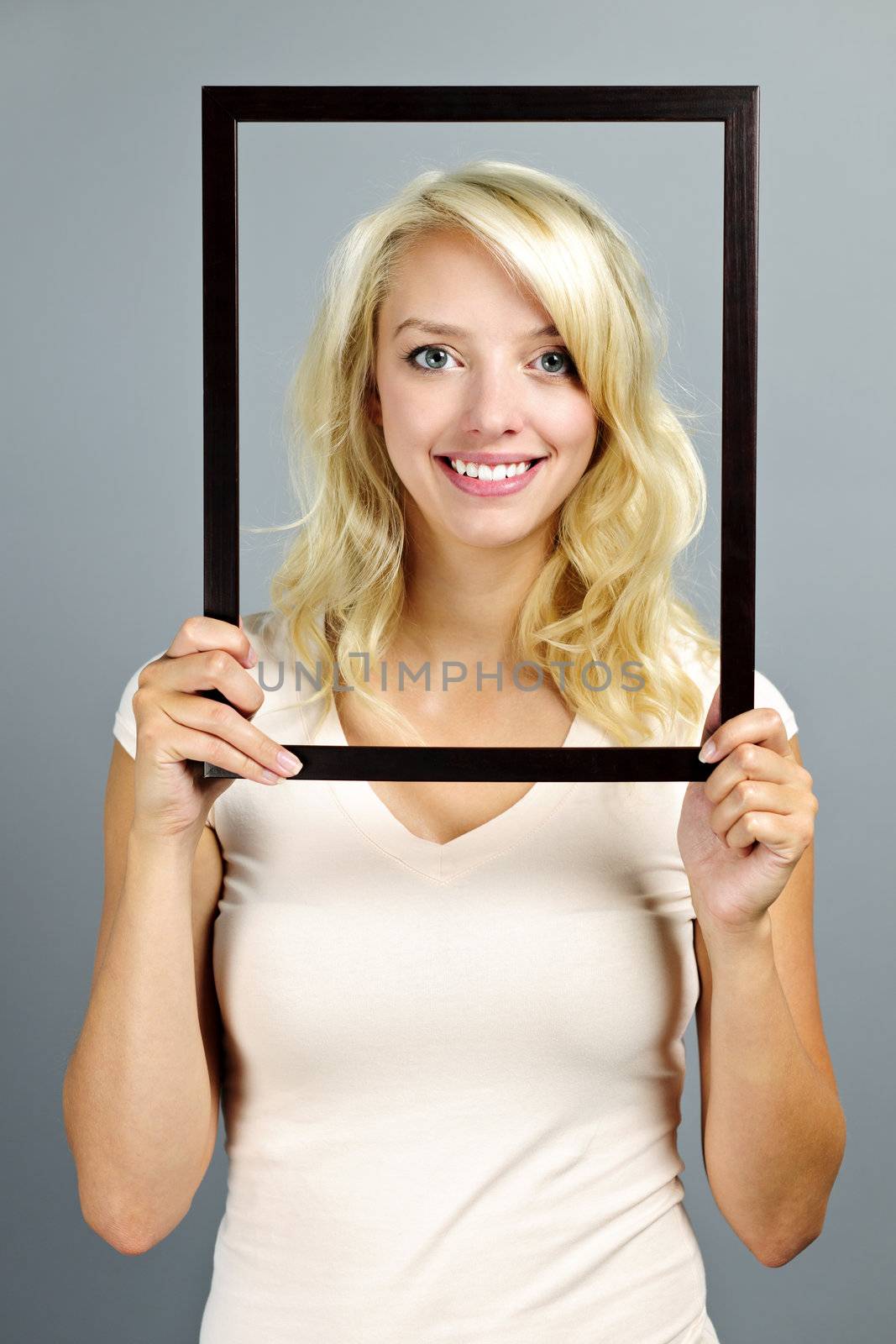 Portrait of smiling young woman holding picture frame on grey background