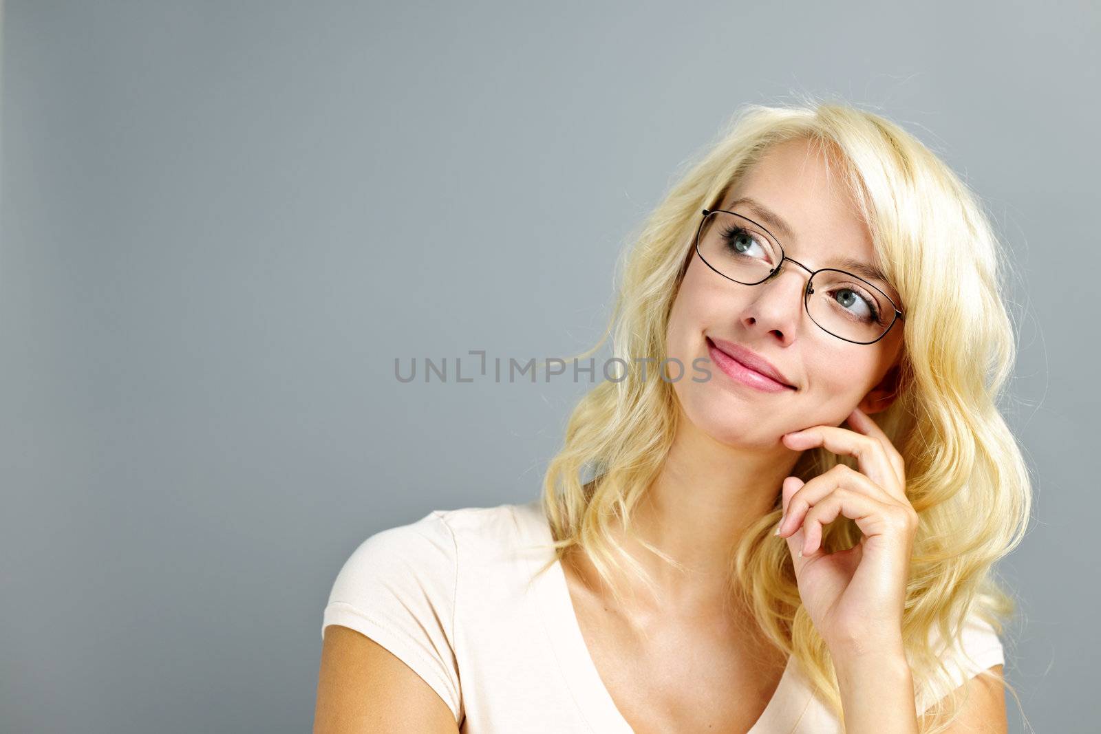Thoughtful young woman wearing eyeglasses on grey background looking up