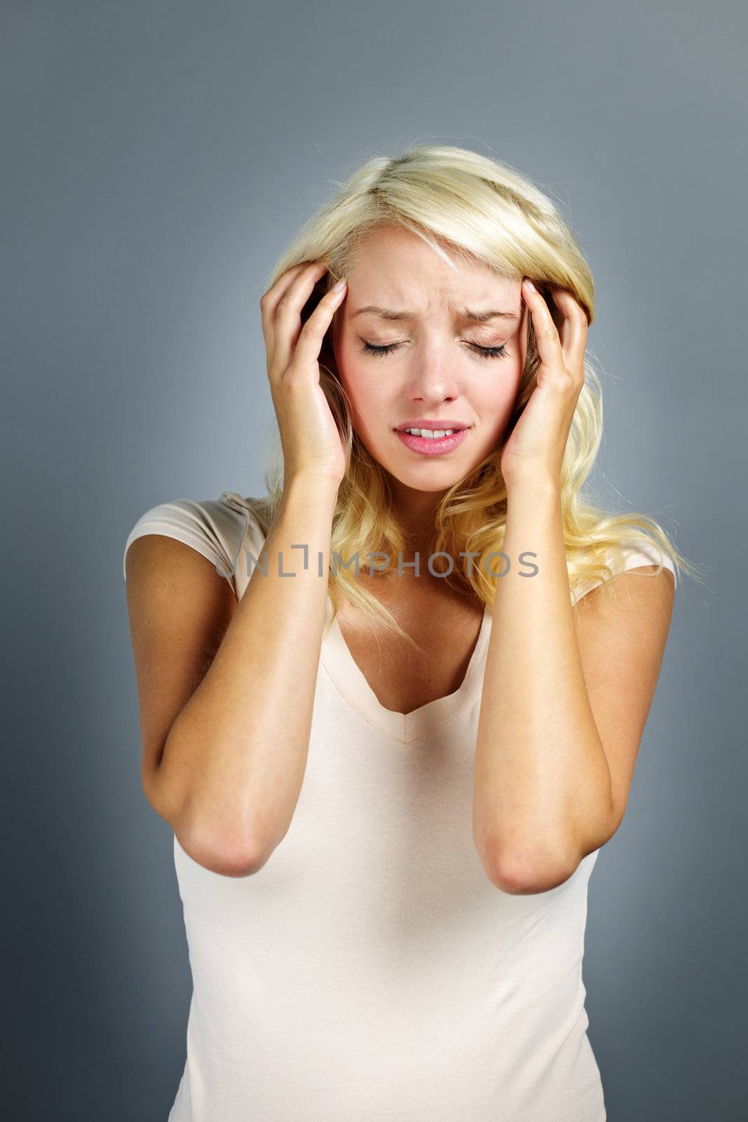 Upset young blonde woman with headache on grey background