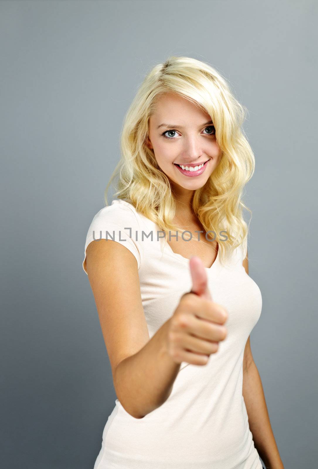 Smiling young blonde woman giving thumbs up on grey background