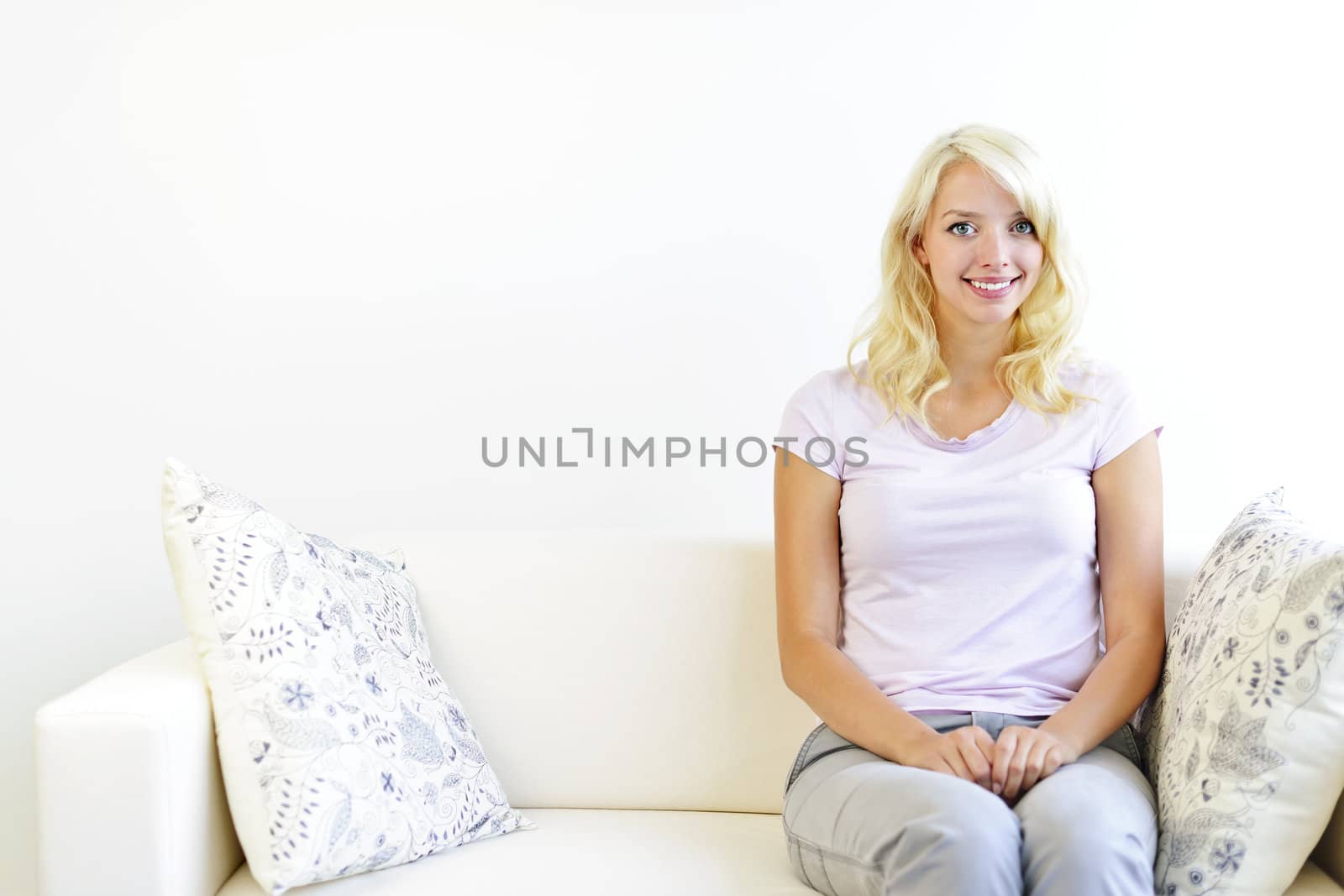 Pretty blonde woman sitting on couch at home smiling