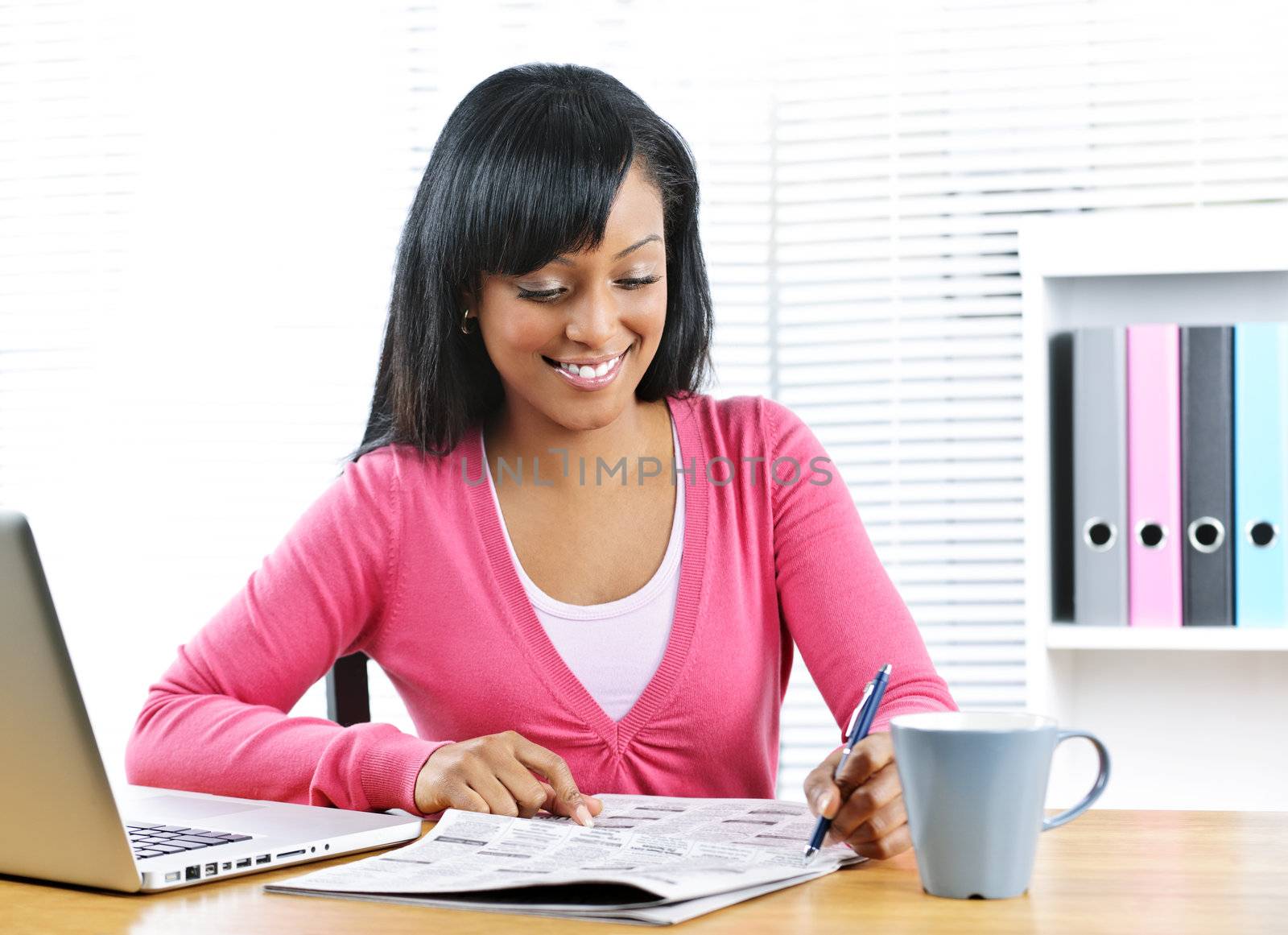 Happy young black female student looking in newspaper for job