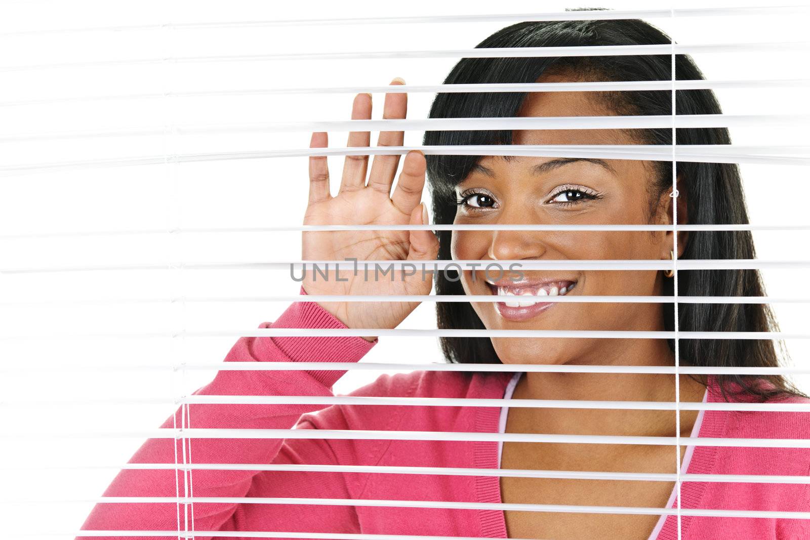 Happy young black woman looking through horizontal venetian blinds