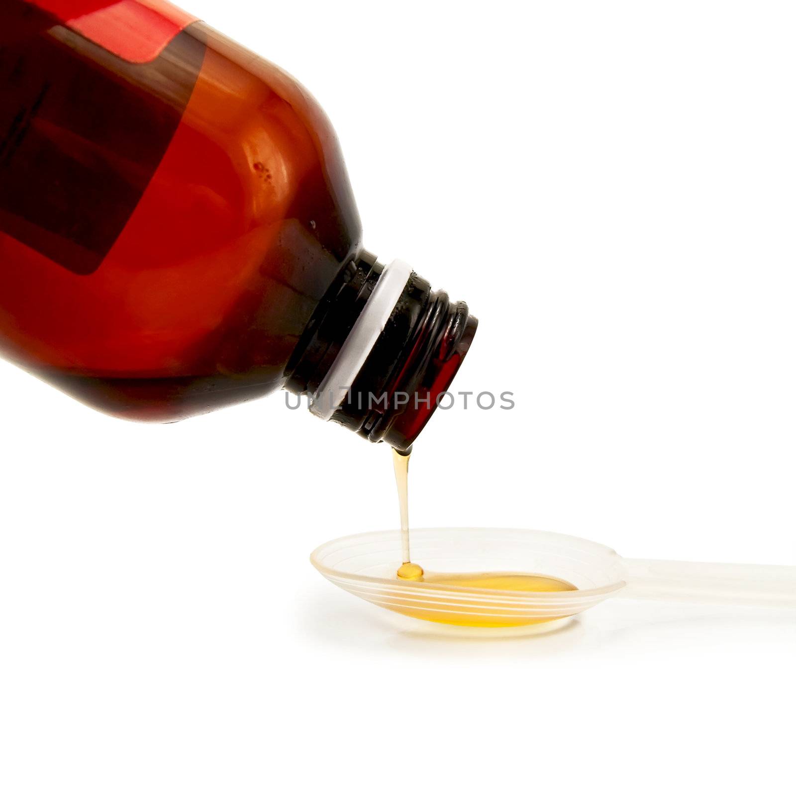 Yellow syrup poured from a brown bottle in a plastic spoon isolated on white background