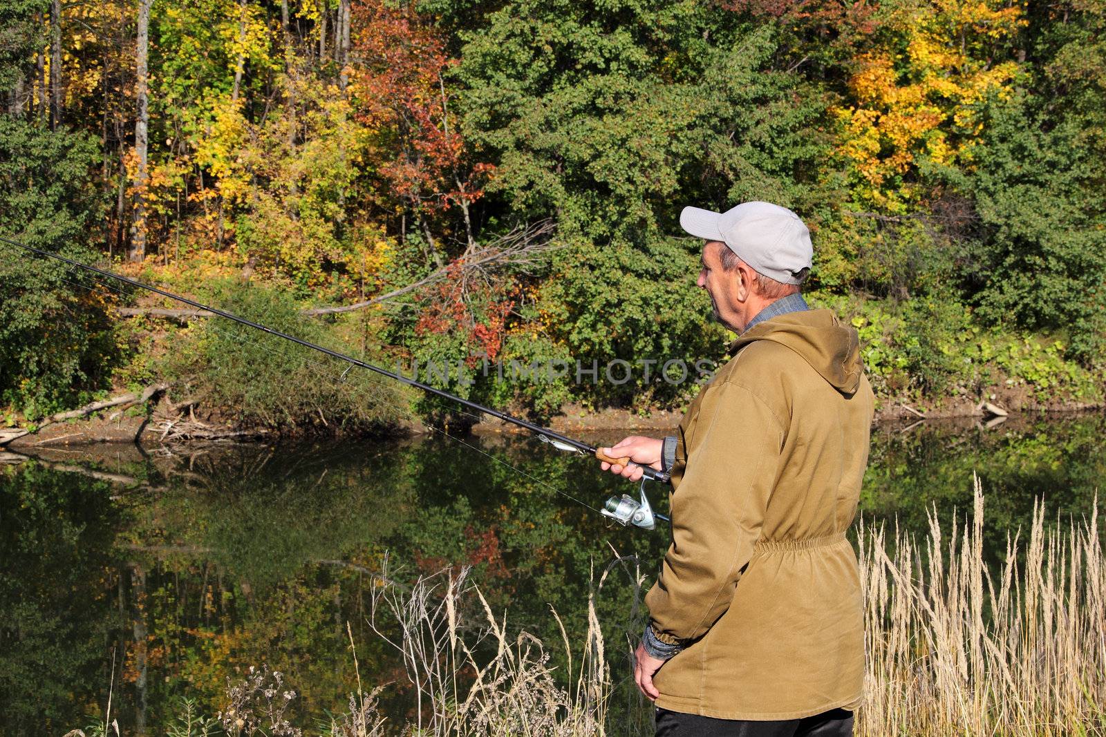 old fisherman with spinning on autumn river
