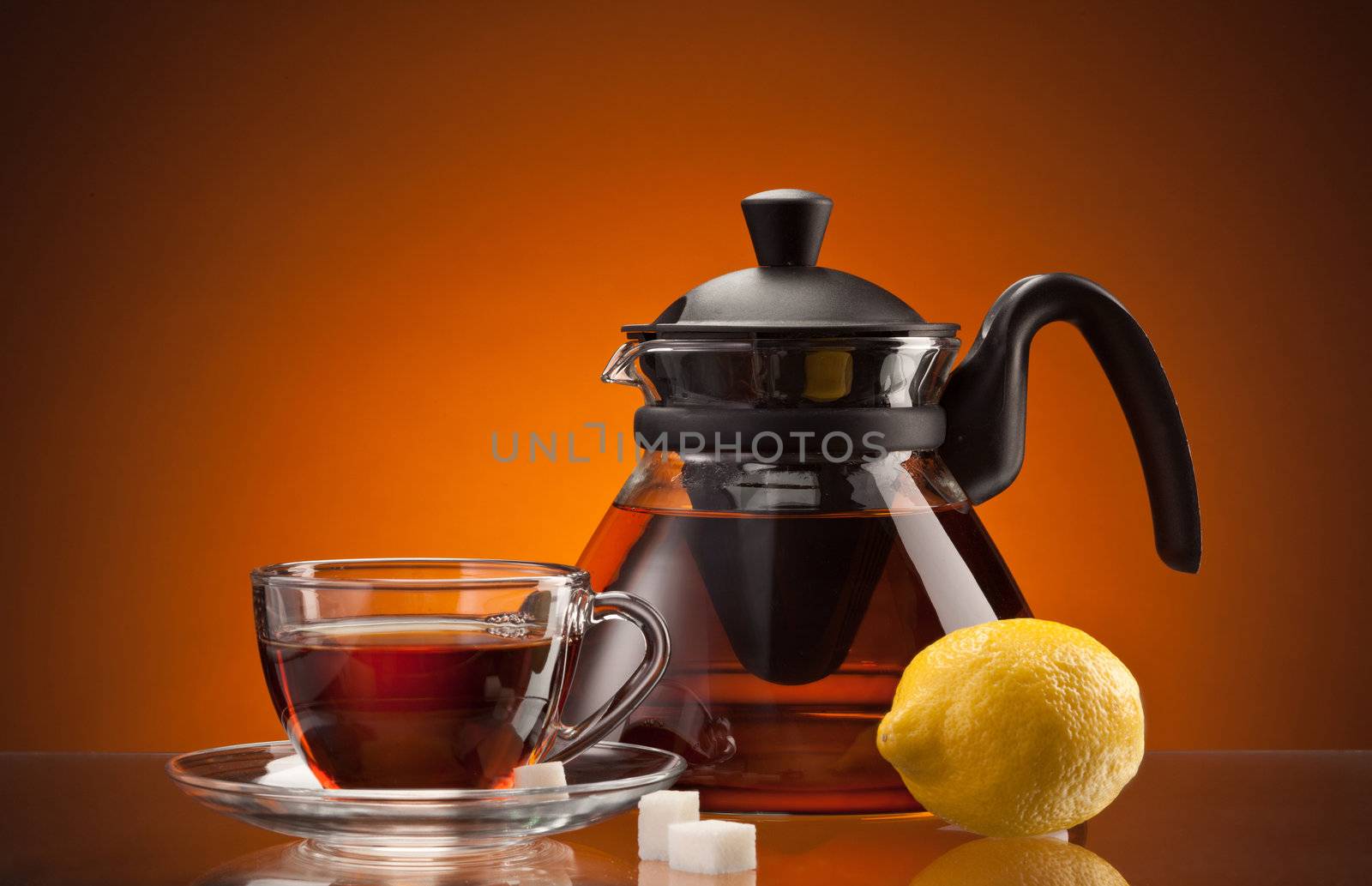 glassy teacup and teapot with tea and lemon over orange