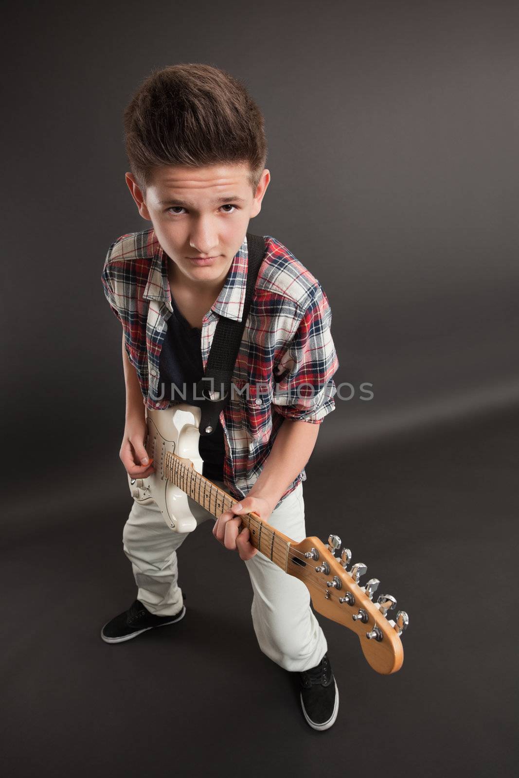 Photo of a teenage male playing a white electric guitar. Taken with wide-angle lens.