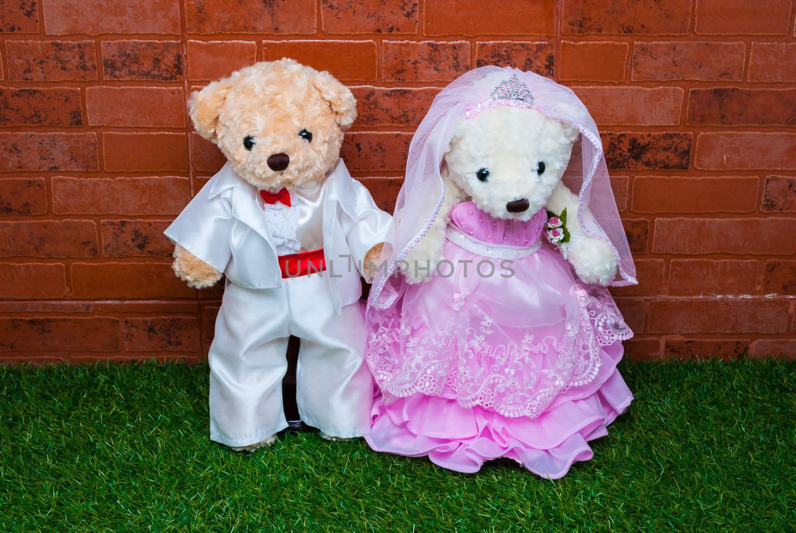 Bridal pair of teddy bear with grass and brick wall.