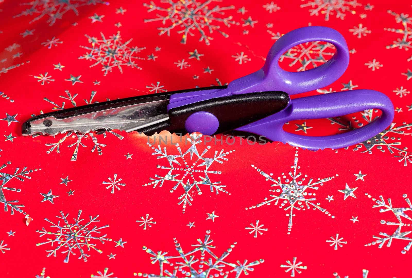Christmas paper being cut by special scissors to create pattern in the cut edge