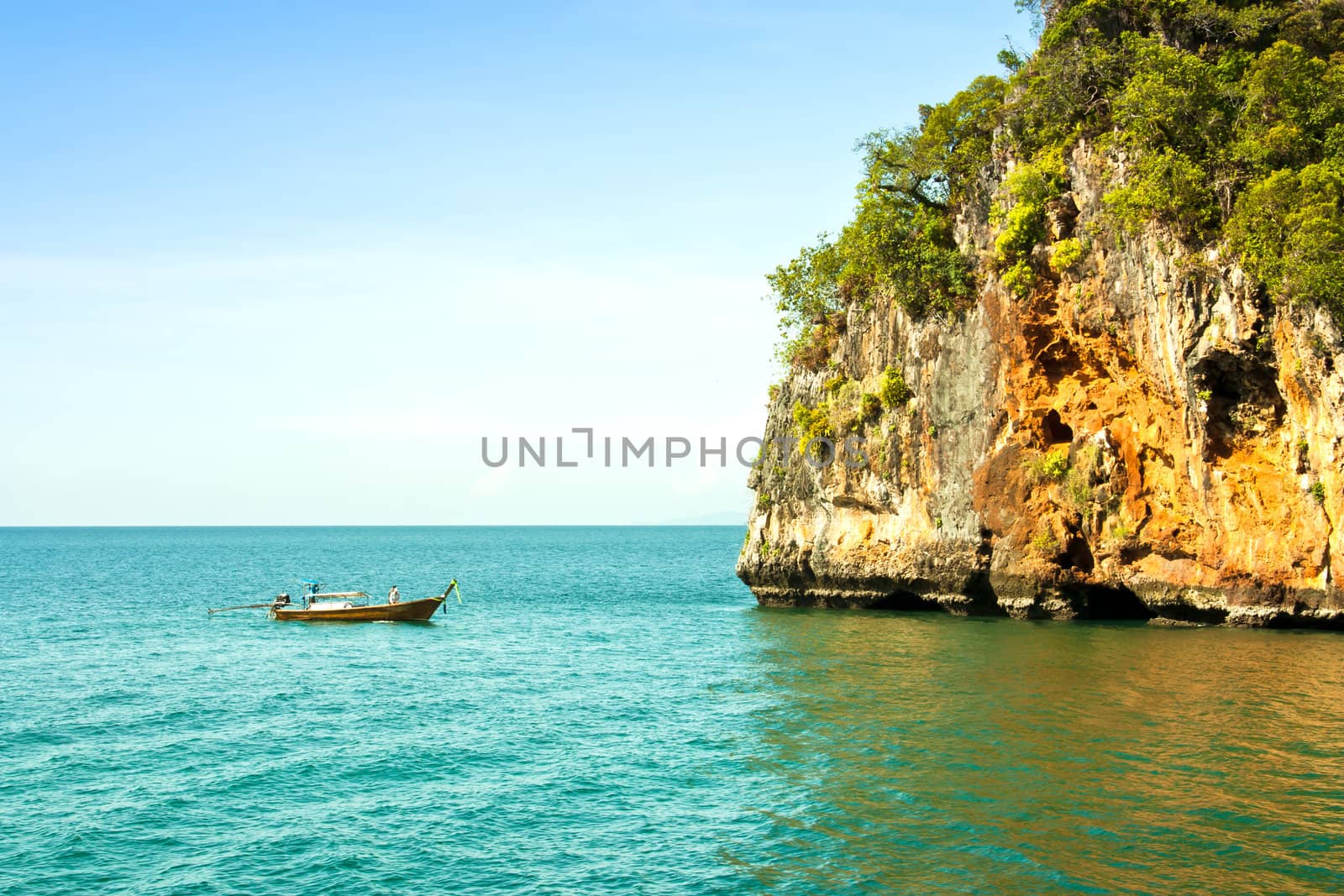 The mountain is a large rock in the sea with fishing boats . In southern Thailand.