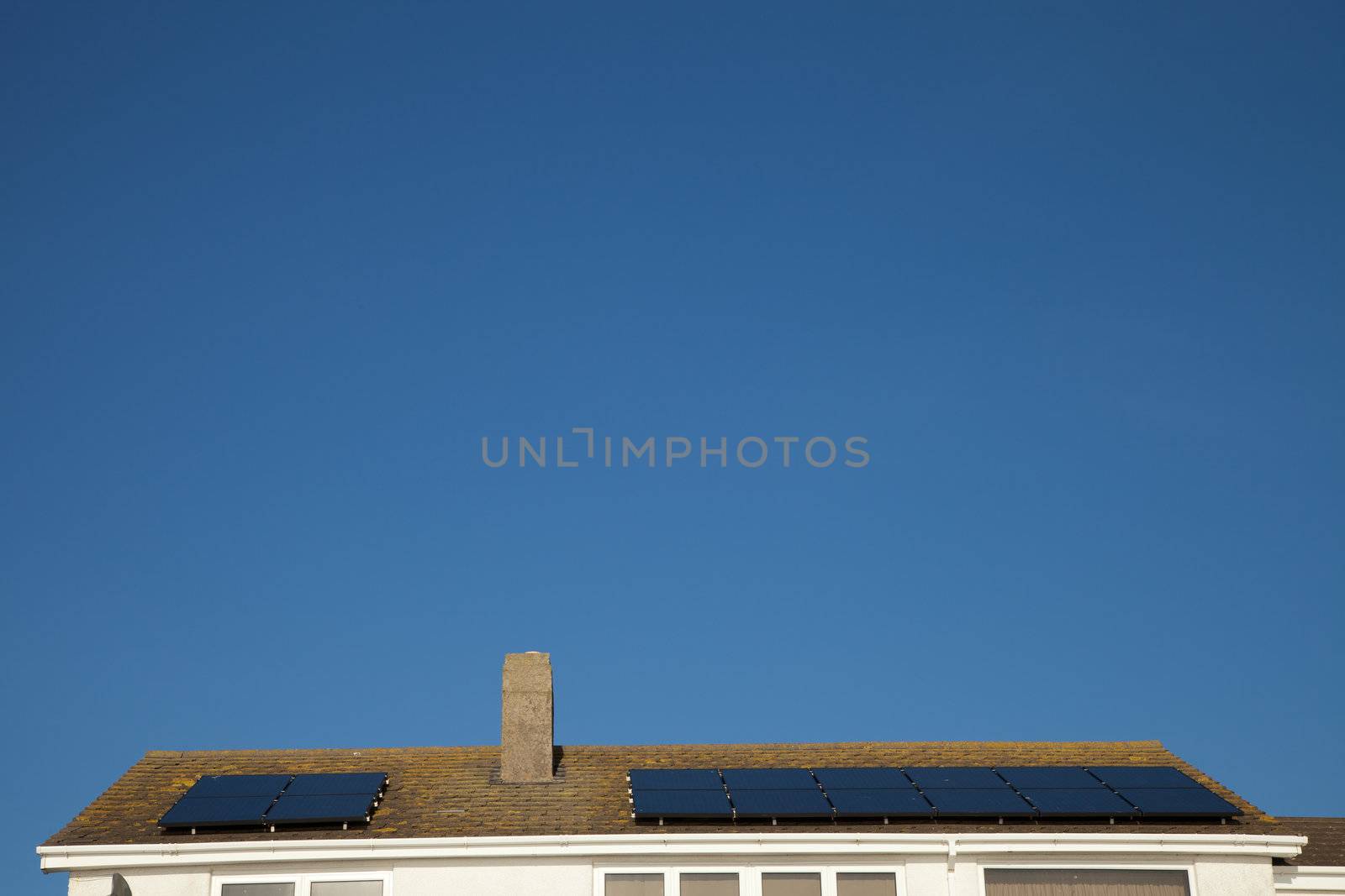 A house roof with an array of solar panel units against a clear blue sky.