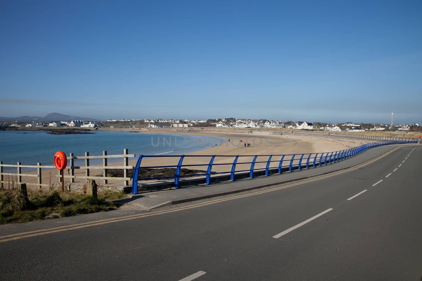 A path and railings curve around the sandy beach of Trearddur bay, Anglesey, Wales, UK.